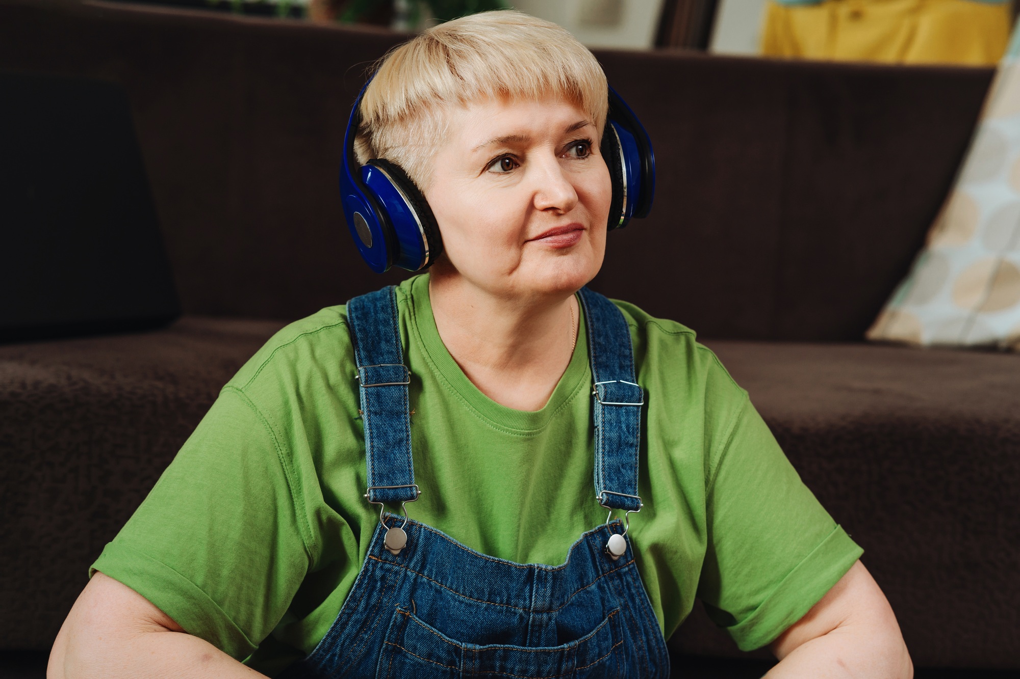 Mature caucasian woman listening to relaxing music through headphones at home