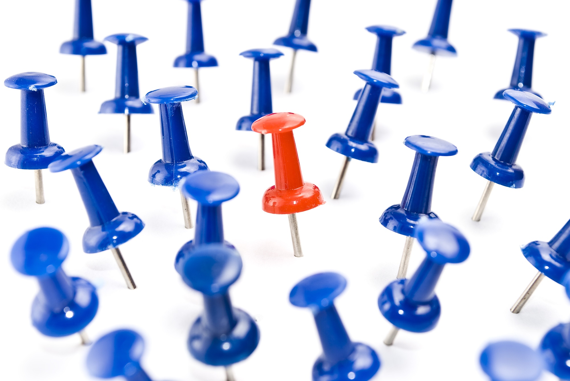 One red thumbtack amid blue thumbtacks. Selective focus