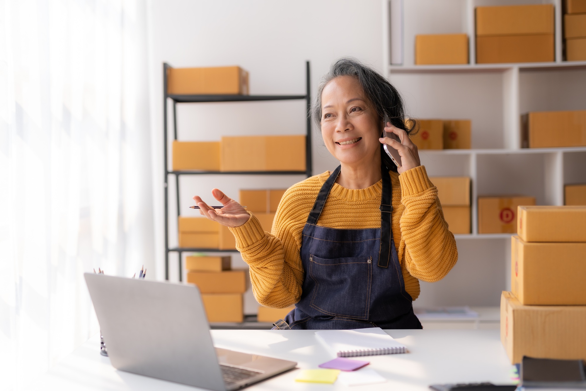 Online owner, Asian senior woman talking on the phone with a customer to track the delivery.