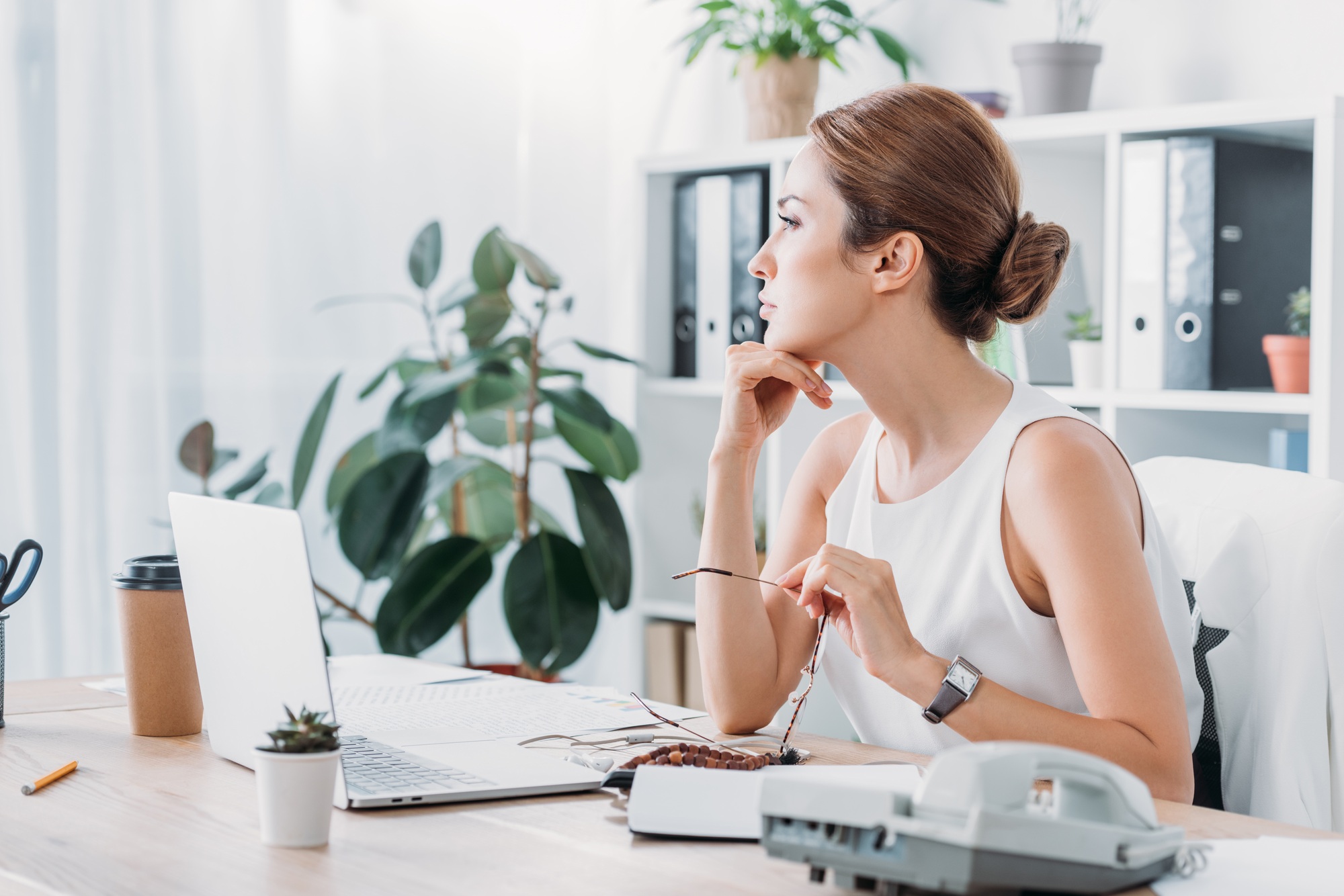 pensive businesswoman sitting at workplace with laptop in modern office