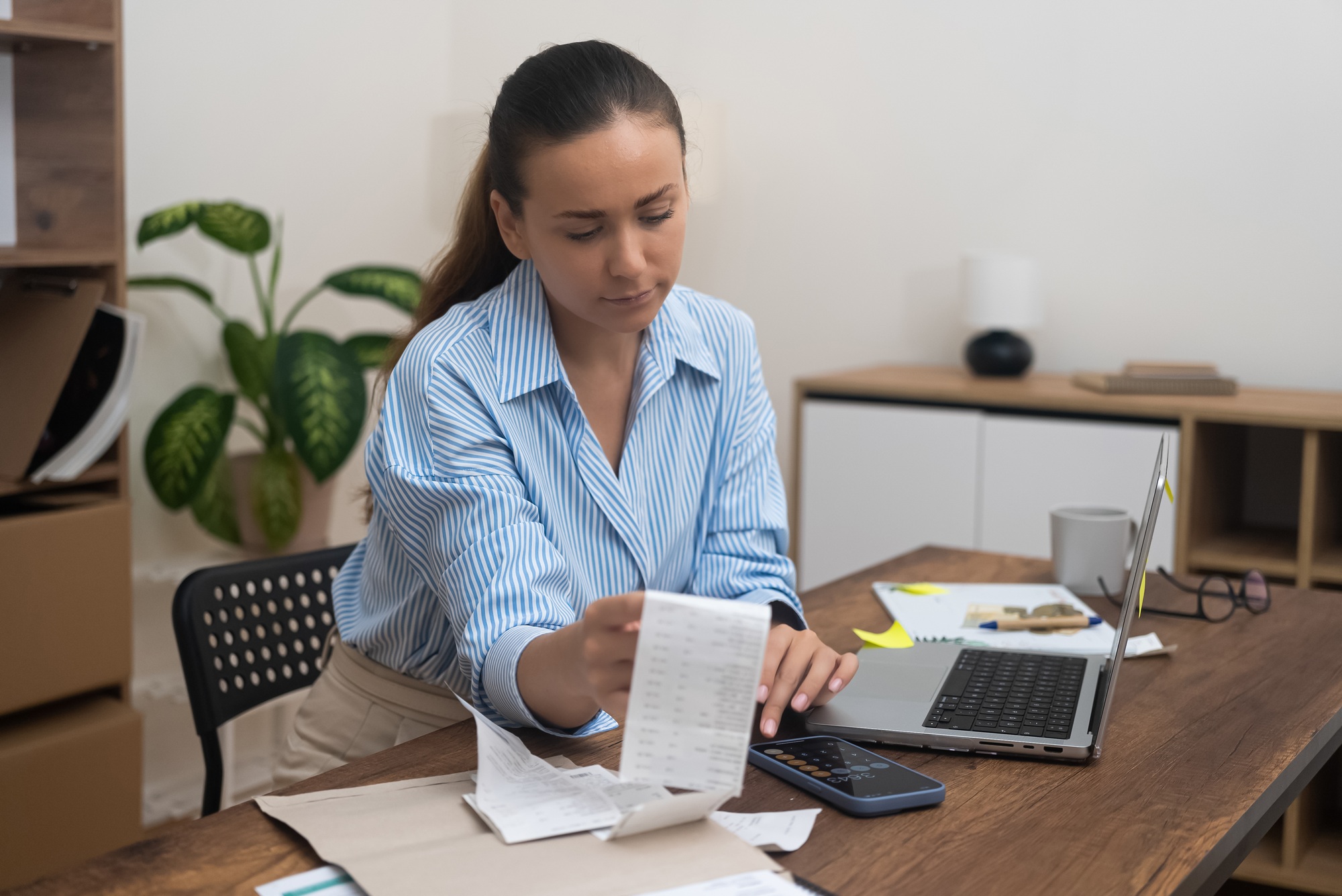 Serious female office employee calculates on calculator with document in hand summarizing taxes