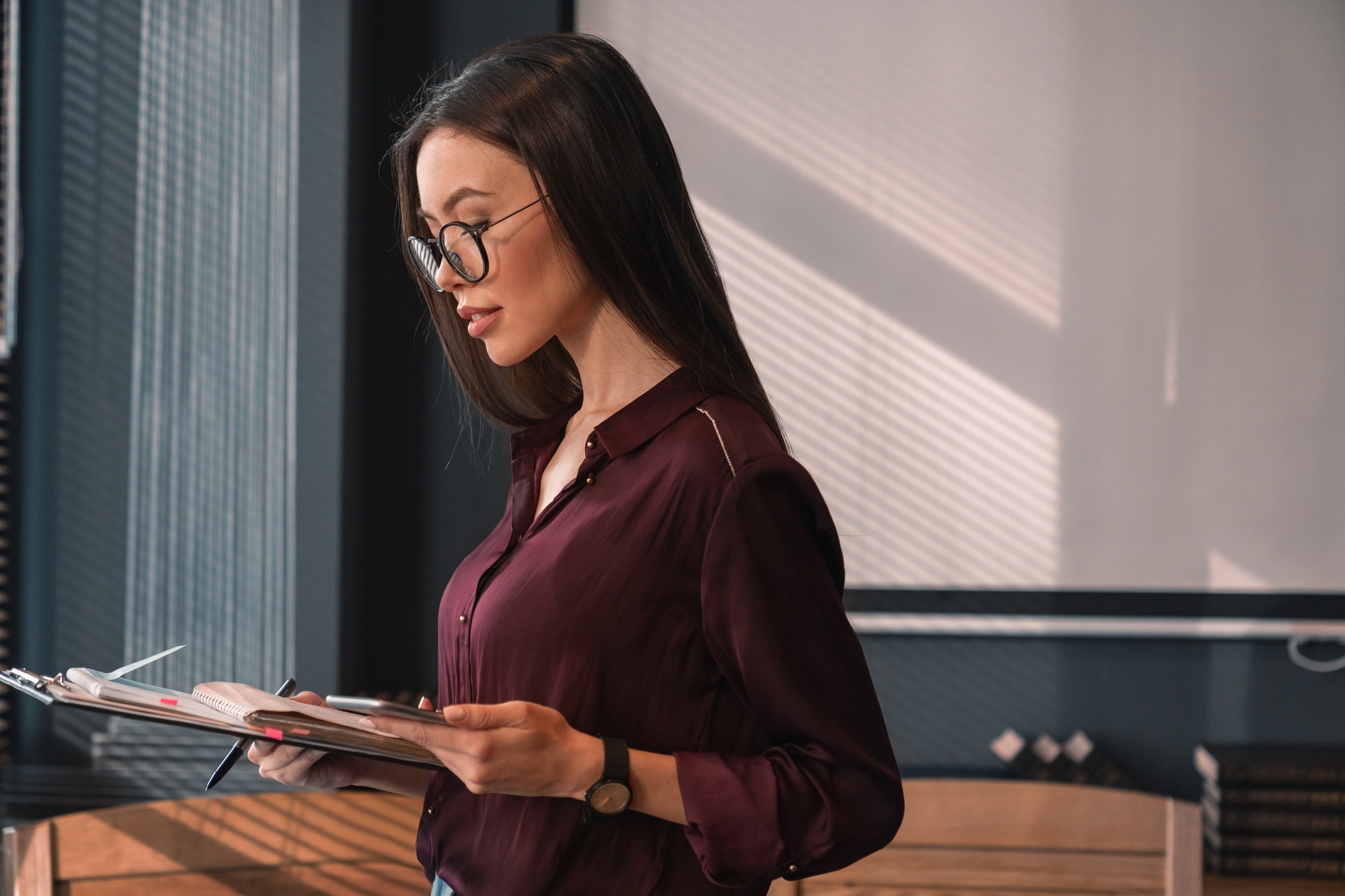 Side view shot of concentrated business woman working with documents and mobile phone in office