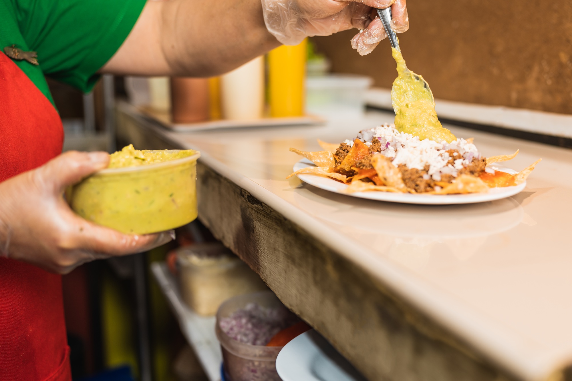 Staff of a kitchen adding sauce to a dish of nachos