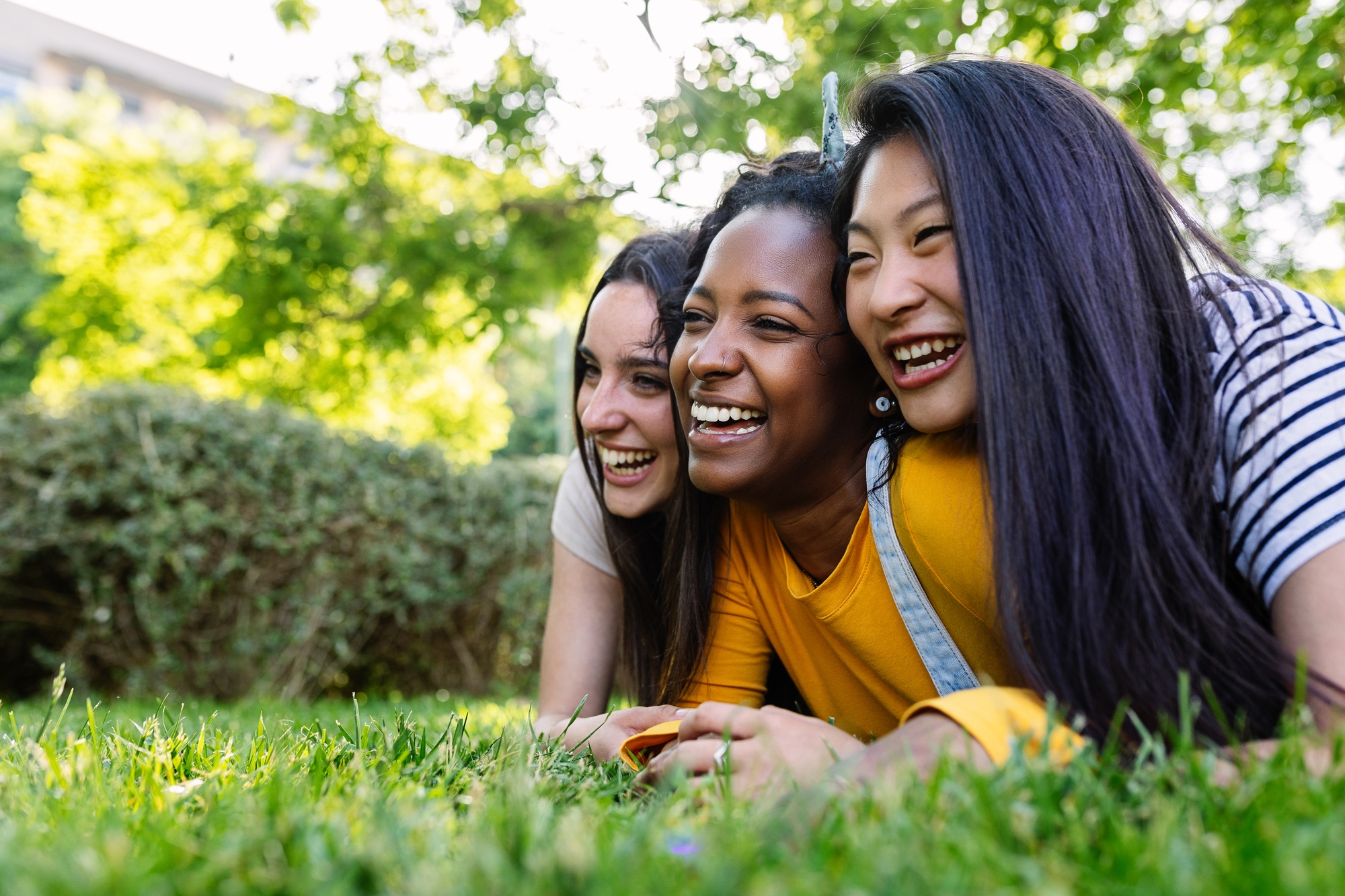 Three young millennial women lying down on the grass at city park