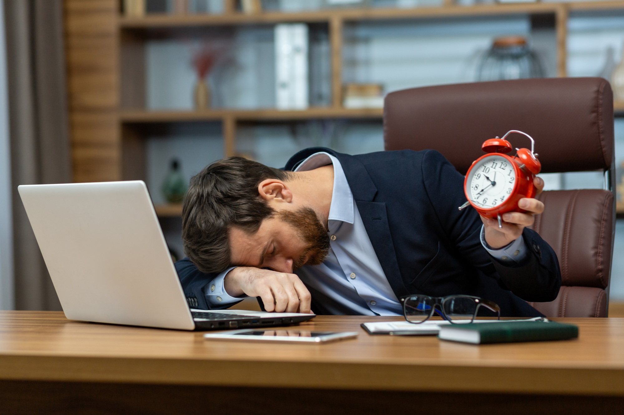 Tired office manager laying down on folded hand on table with personal gadgets and holding red