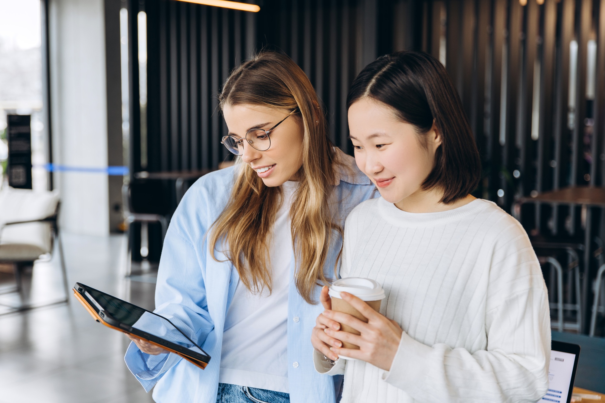 Two young businesswomen using digital tablet and drinking coffee in office