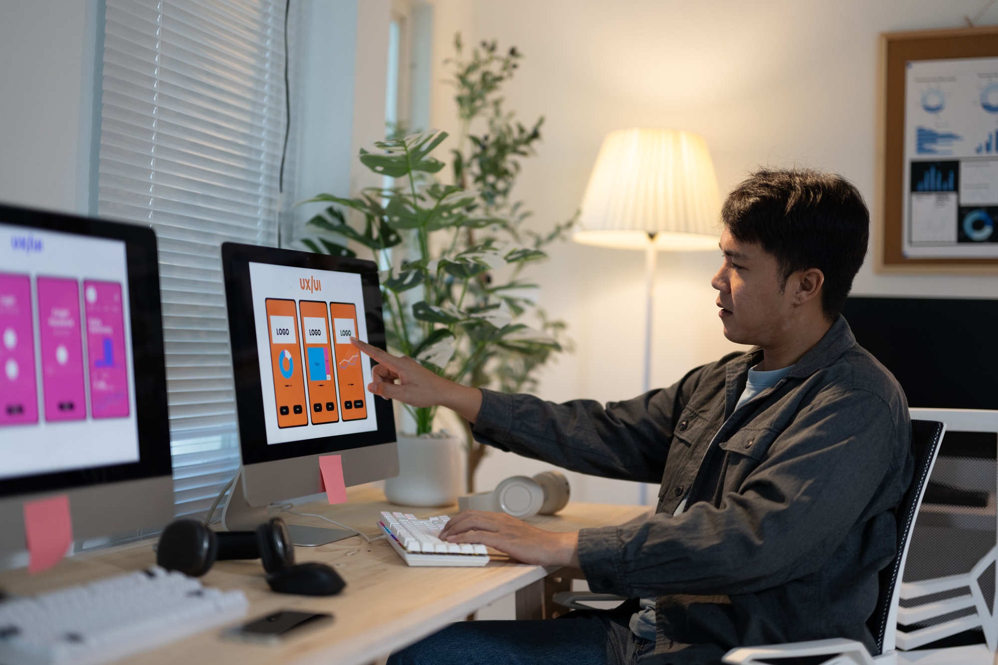 Ui designer is working late, reviewing the design of a mobile app on his computer. He is pointing at