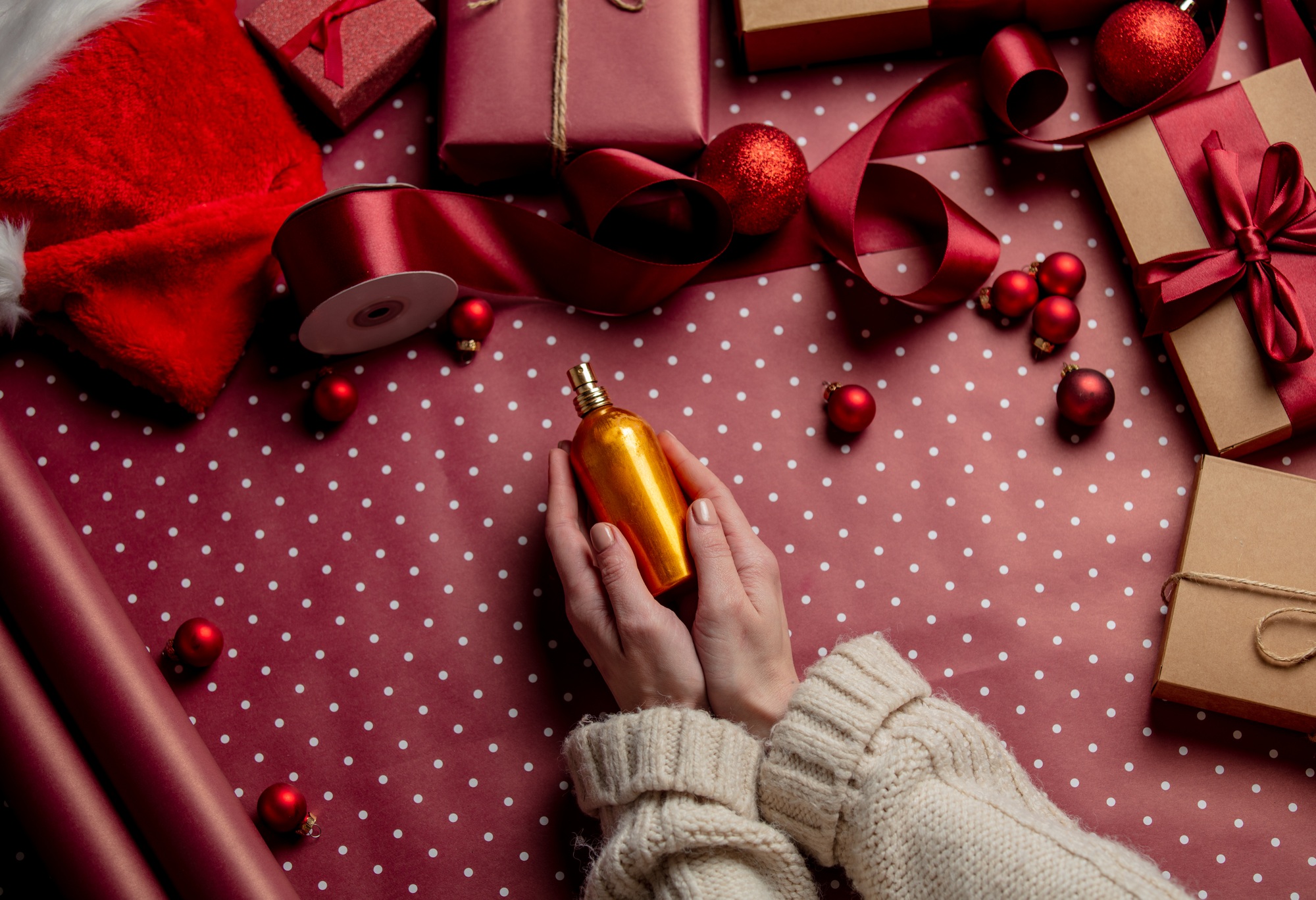 Woman hands hold perfume near gifts on wrapping paper