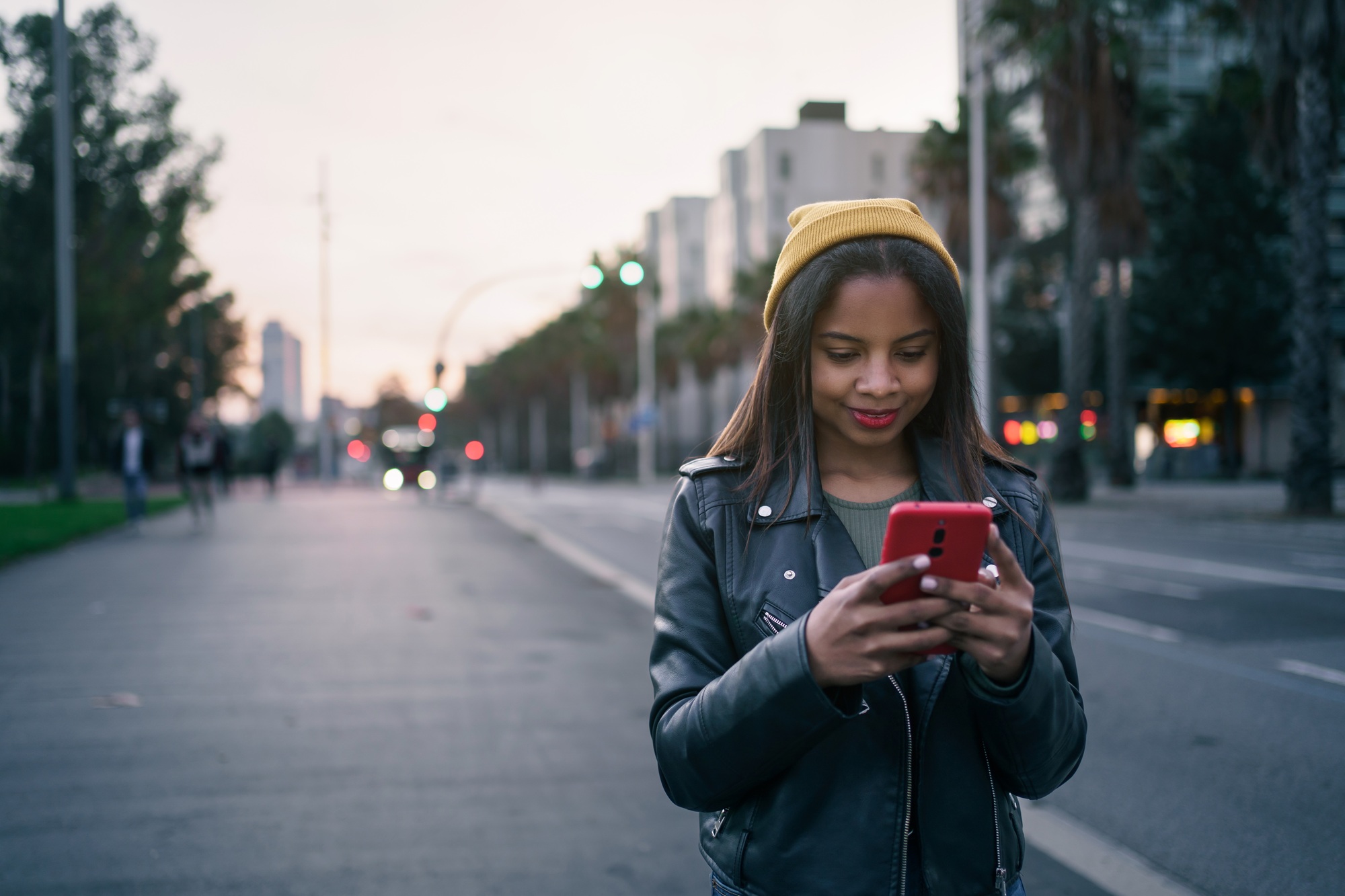 young African American Woman in stylish leather jacket messaging with smartphone
