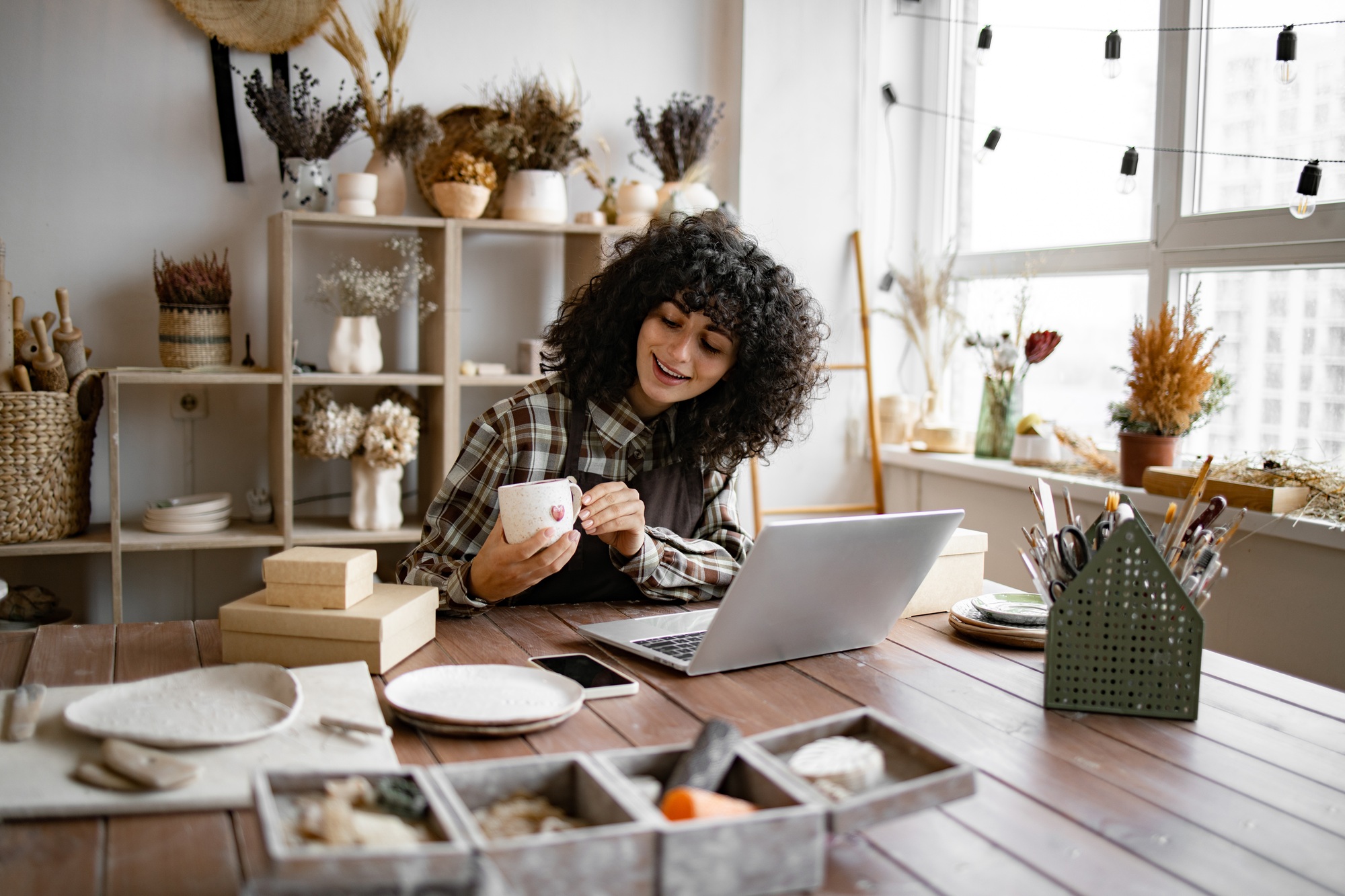 Young ceramic shop owner using laptop while working in store.