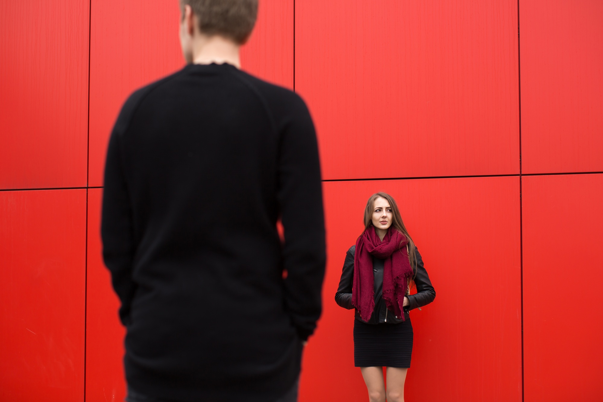Young man and woman in passion, emotion, on the street with a backdrop of the red wall. Fashion