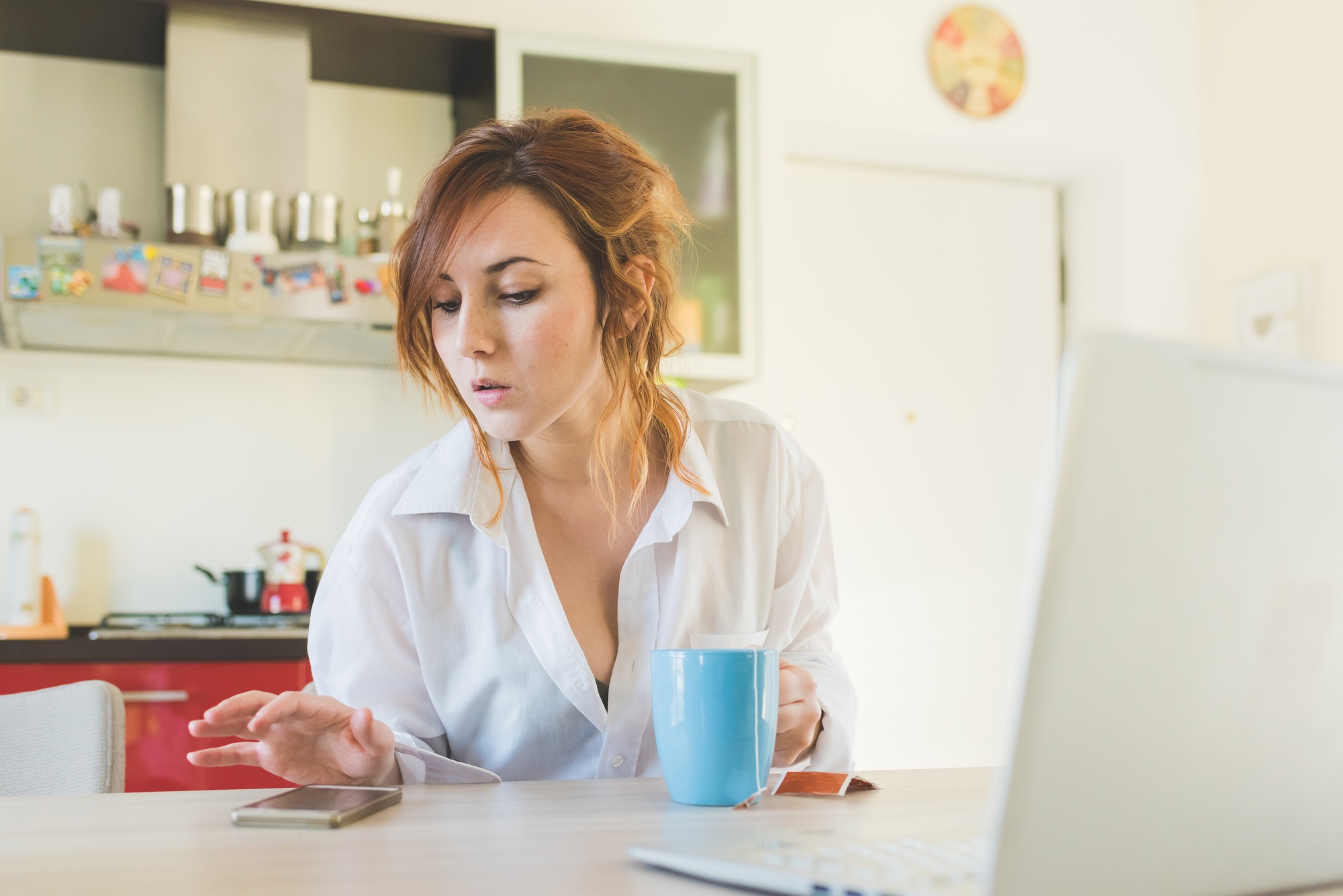 Young woman at kitchen table looking at smartphone