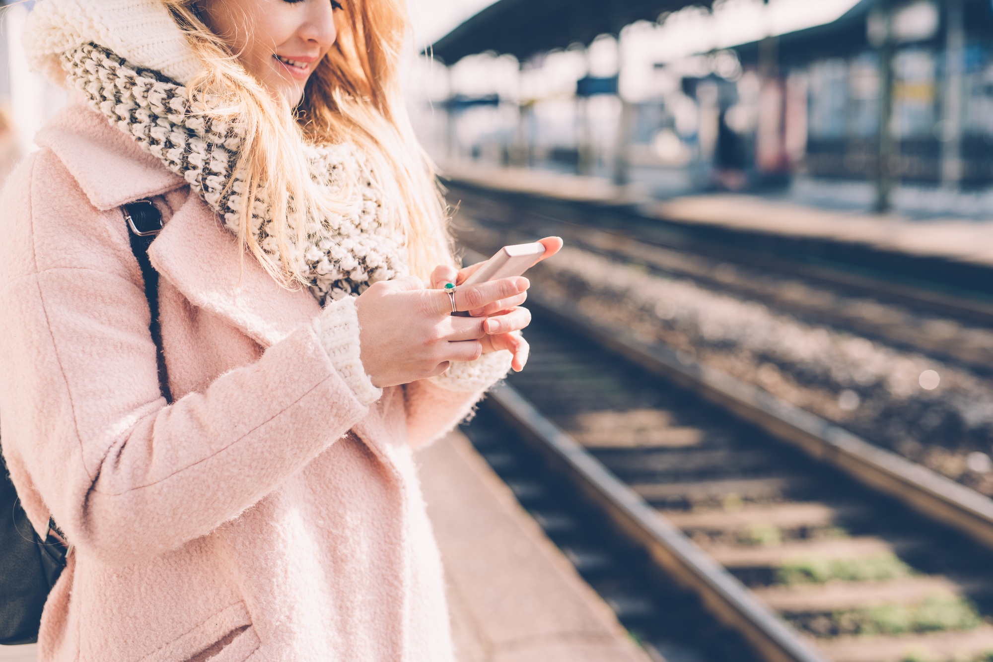 Young woman at the train platform using smart phone hand hold