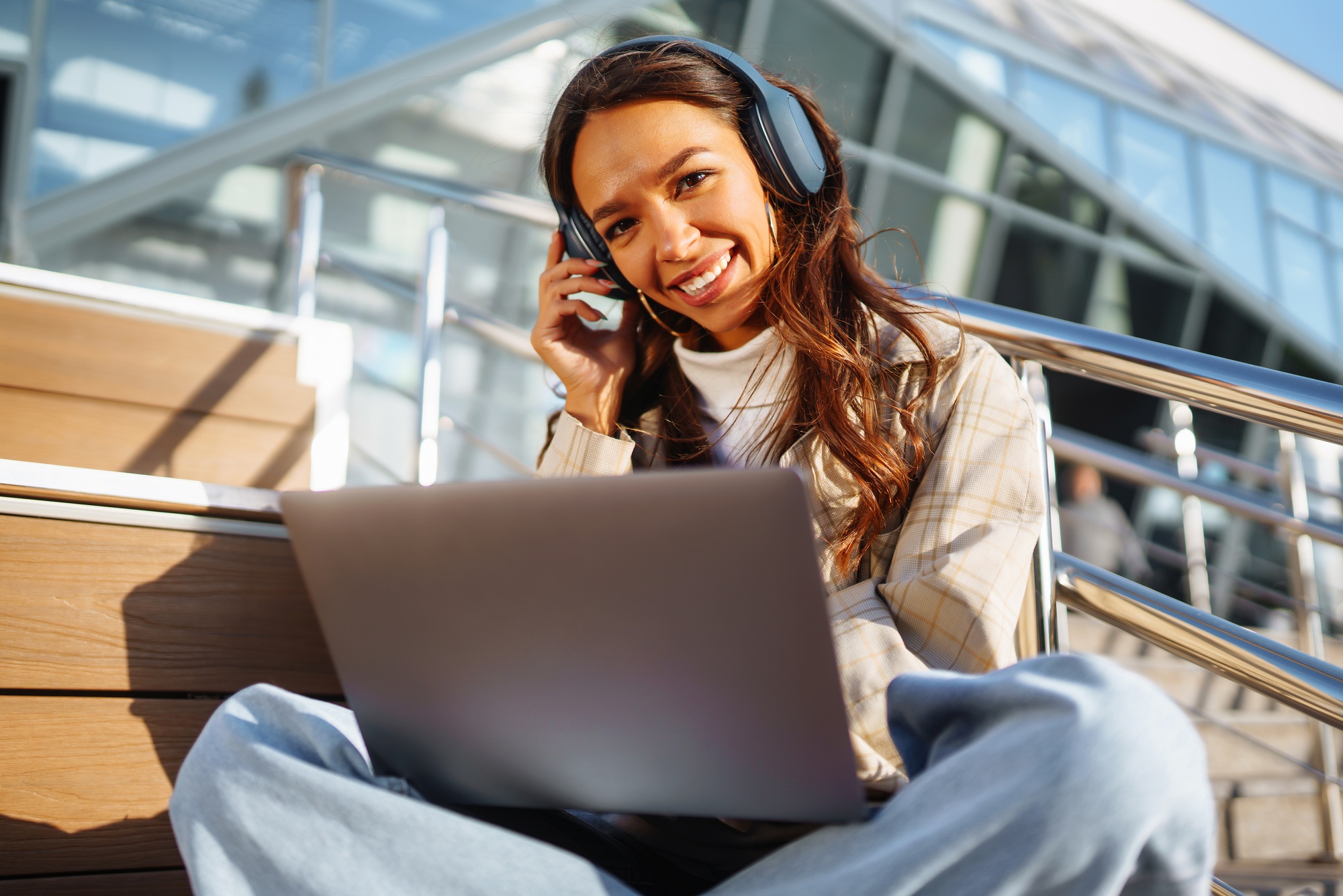 Young woman in headphones with laptop on city street. Video conference. ?nline training. Freelancer