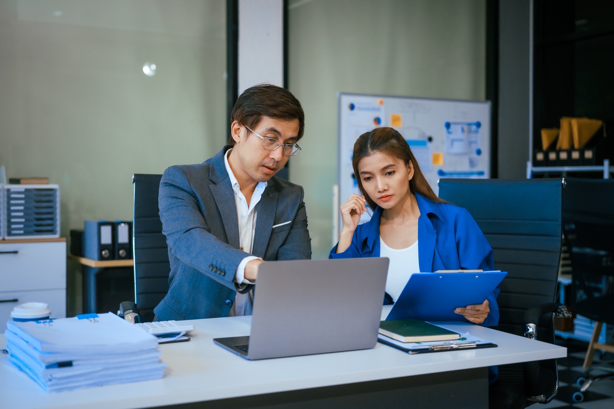 A stressed businessman and woman sit at a desk,overwhelmed by business challenges discuss problems