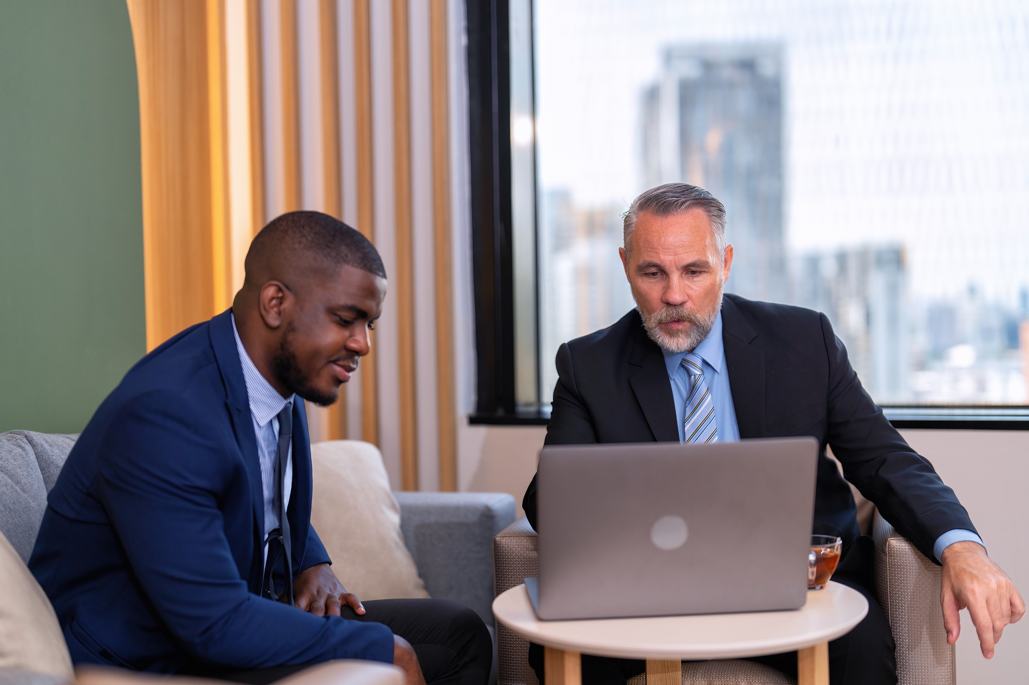 Two businessmen sitting on sofa working discuss on financial forecast together on laptop information