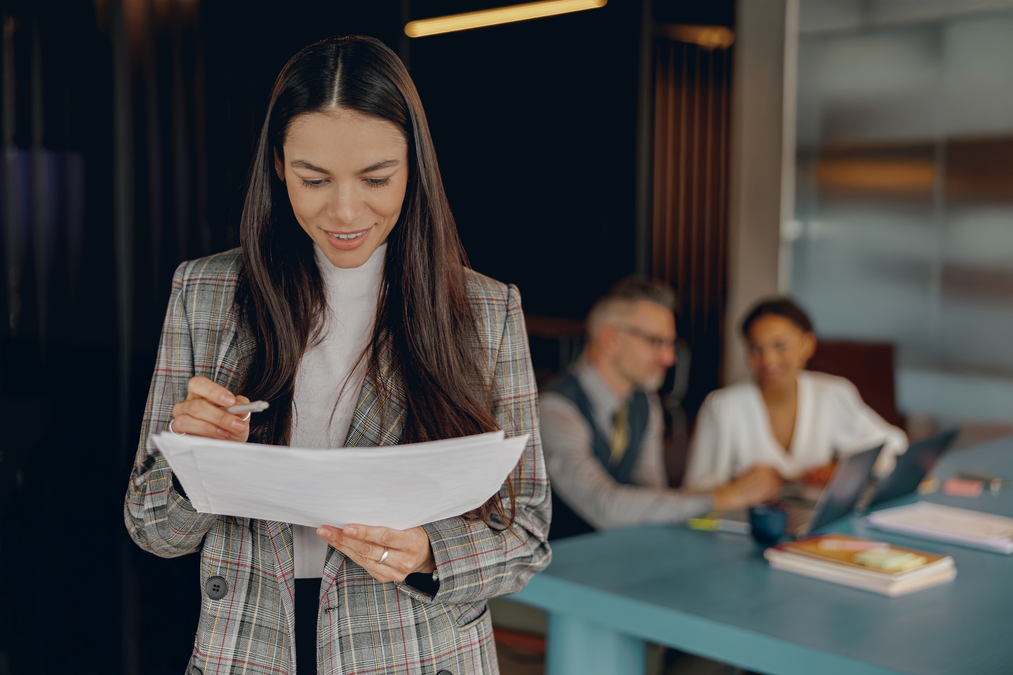 A businesswoman reviews important documents in a modern office, showing her focus and concentration