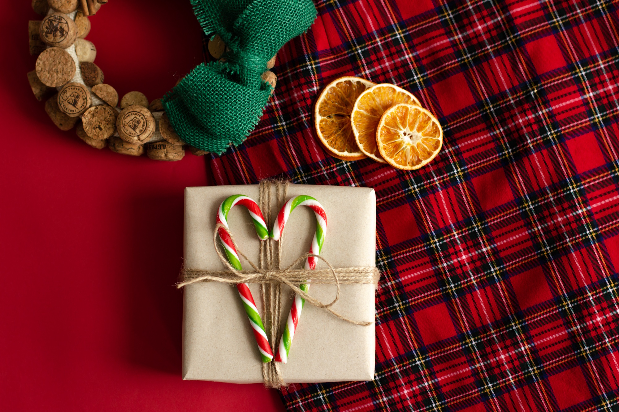 A craft gift box, dried oranges and a handmade wreath with lie on a red checkered background.
