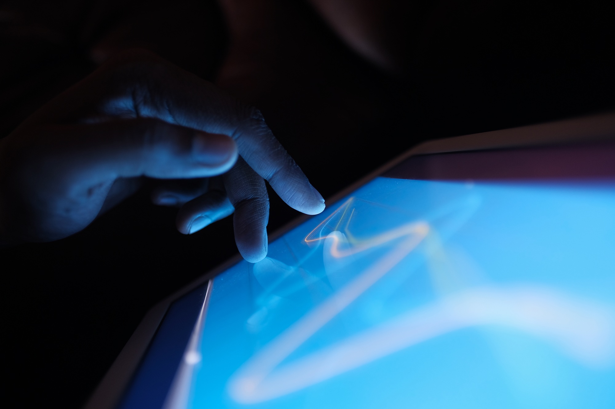A finger gently touches an interactive tablet screen in low light, showcasing modern design