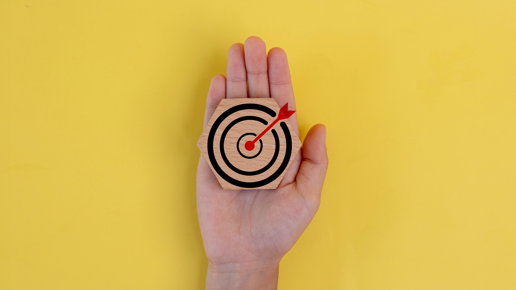 A hand holding a wooden target with a red arrow pointing to the center