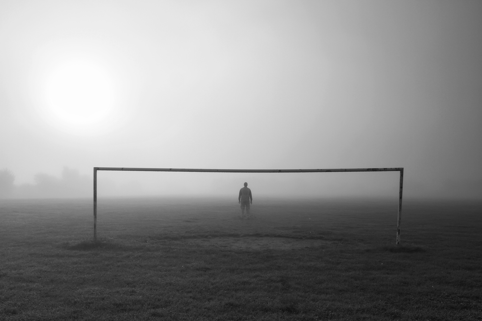 A lone sportsman on a football pitch with goalposts on a foggy or misty day in park life