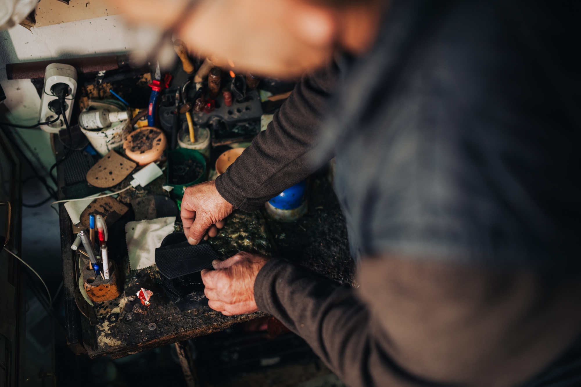 A senior cobbler is gluing sole on shoe at his workshop.