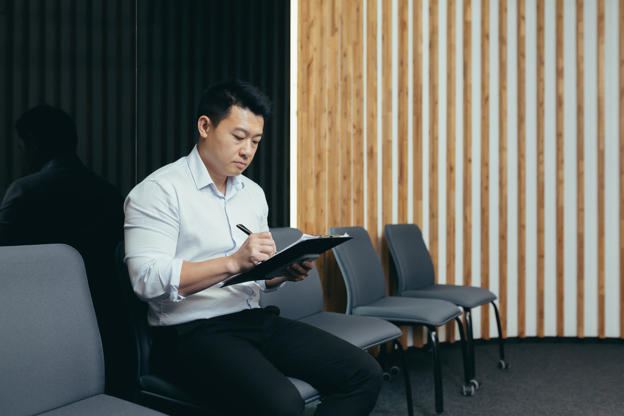 A young Asian man sits in the lobby and fills out a survey questionnaire in the medical center, in