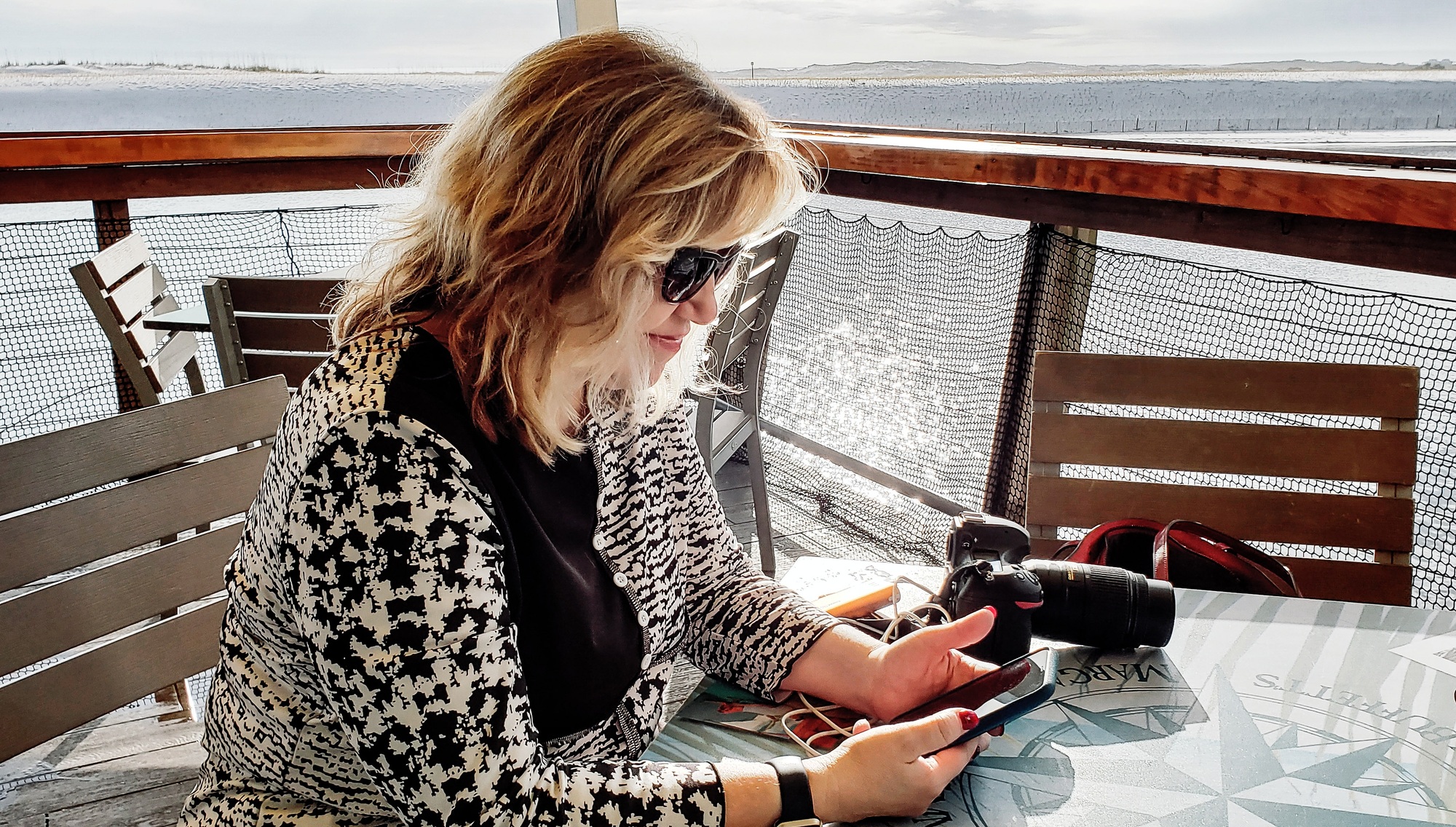 Active baby boomer sitting on a deck on the harbor bay checking Twenty20 on her cellphone for sales