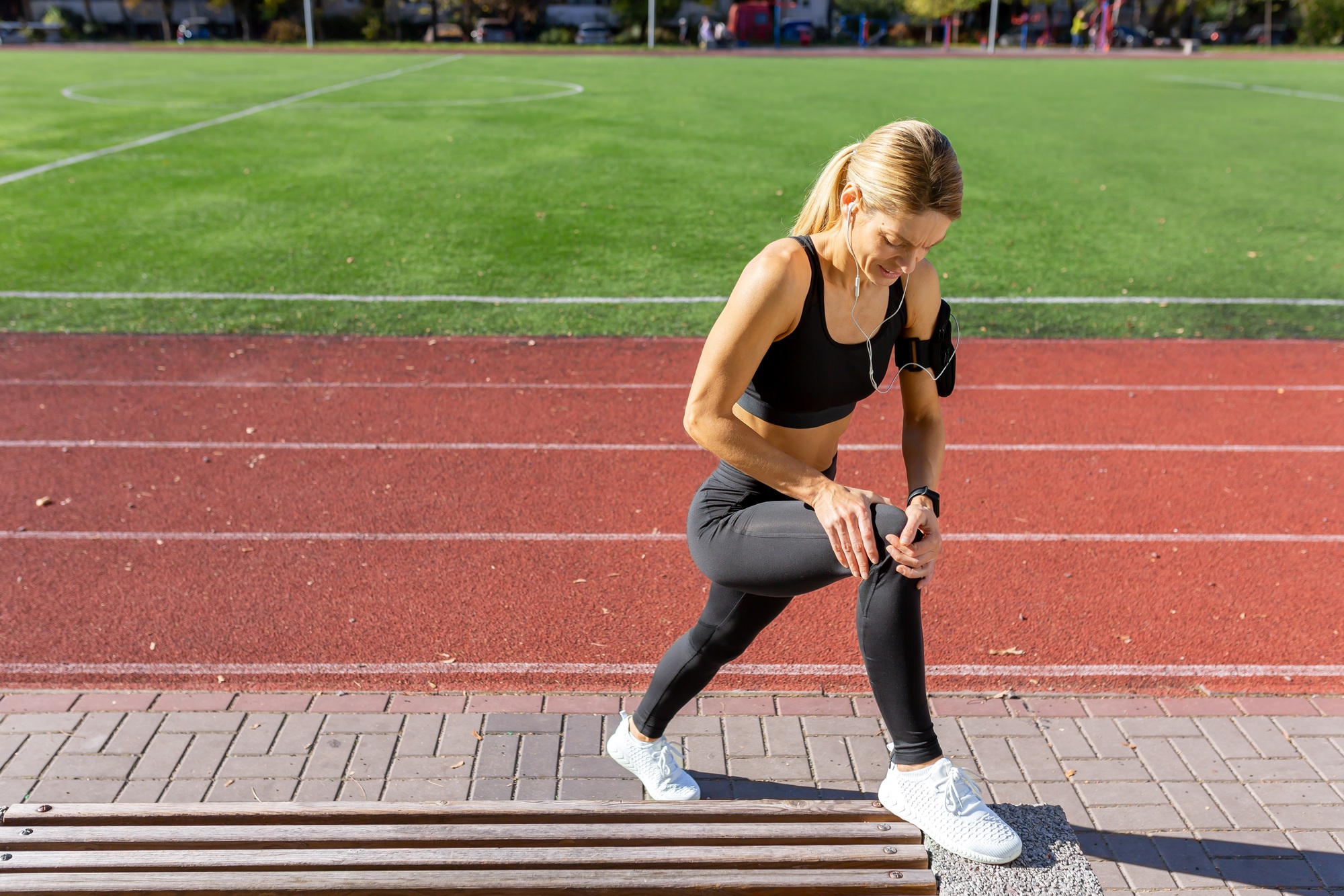 Active woman checking fitness tracker during outdoor workout on track field