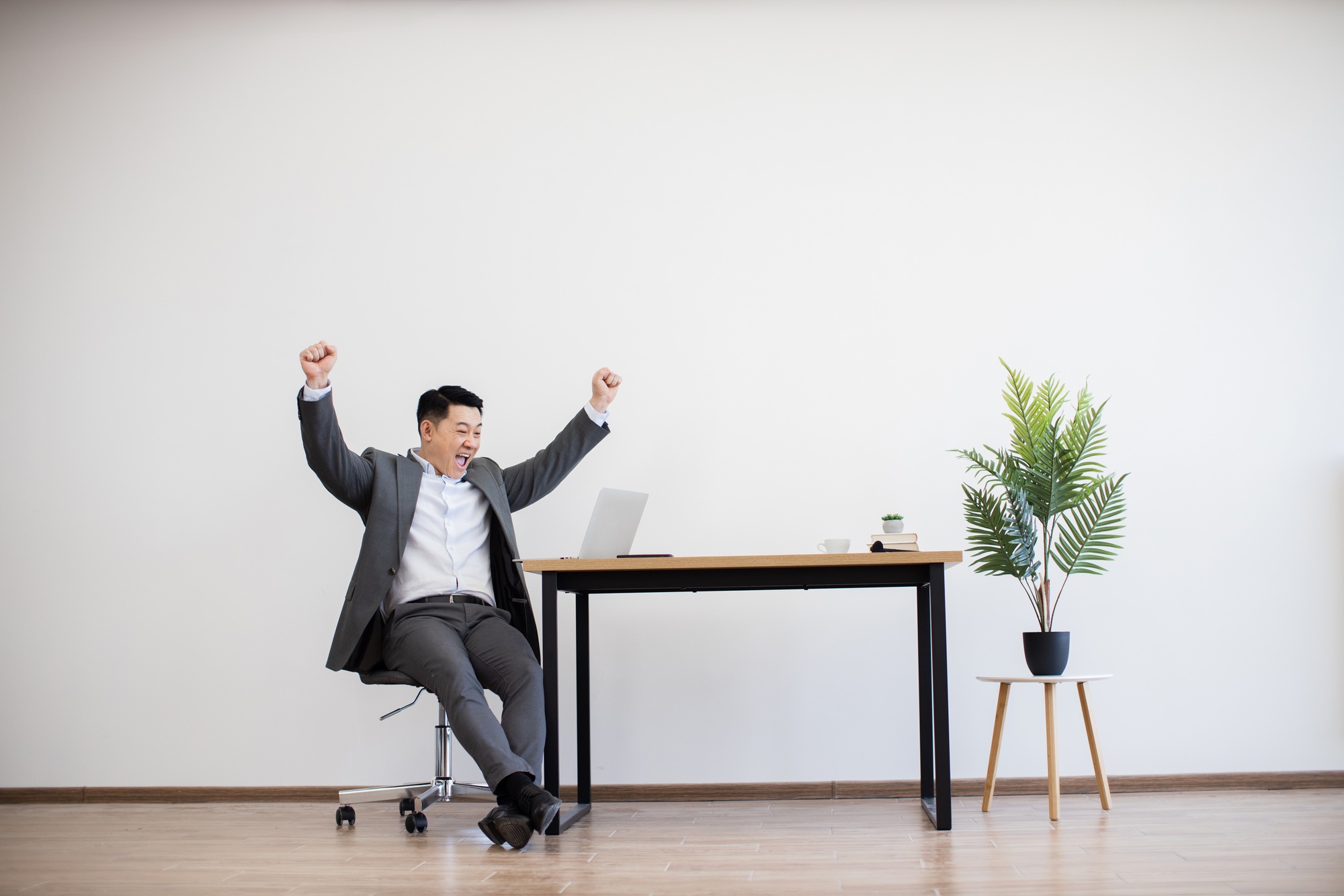 Asian businessman celebrating successful project completion at office desk