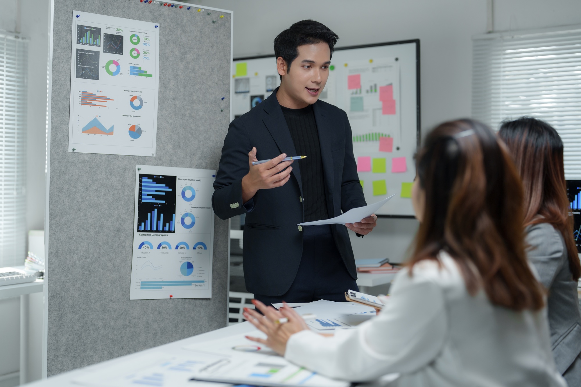 Asian businessman leading meeting with charts and statistics displayed on boards