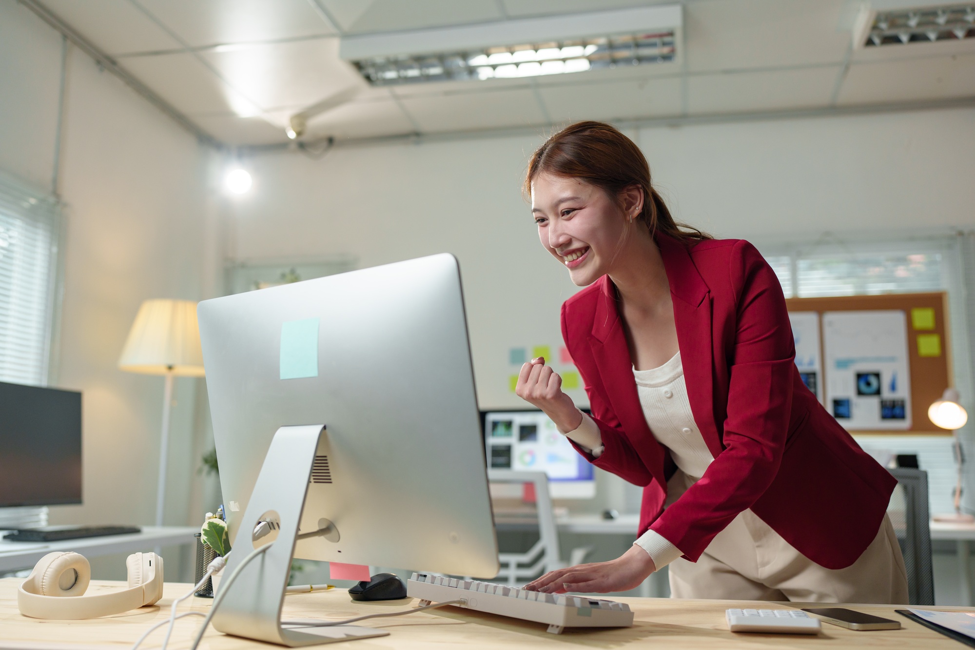 Asian businesswoman celebrating a significant achievement while working at her desk, expressing exci