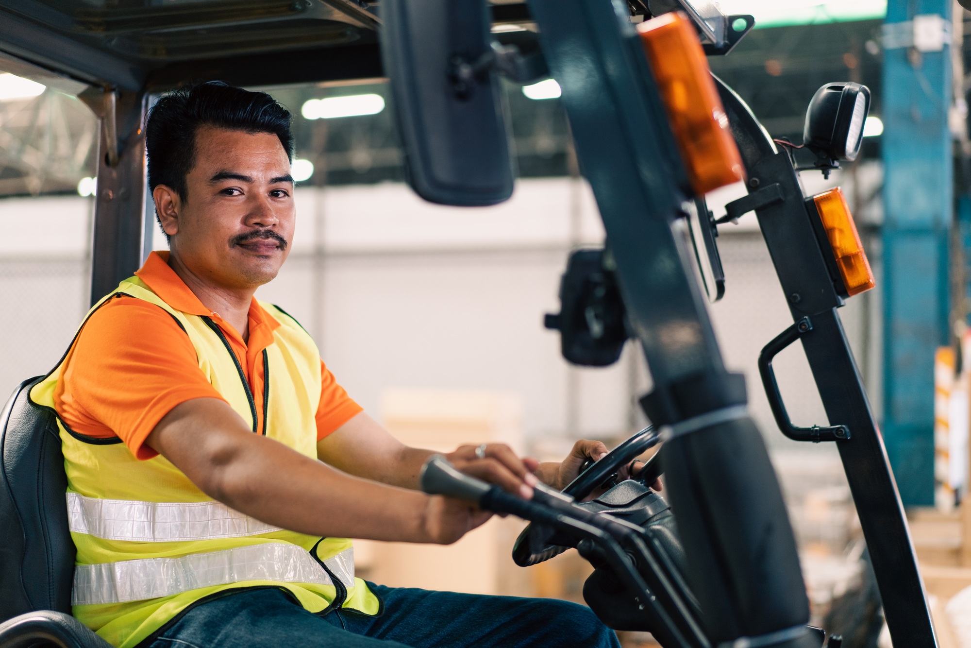 Asian male driver driving forklift to shipping delivery in the warehouse distribution