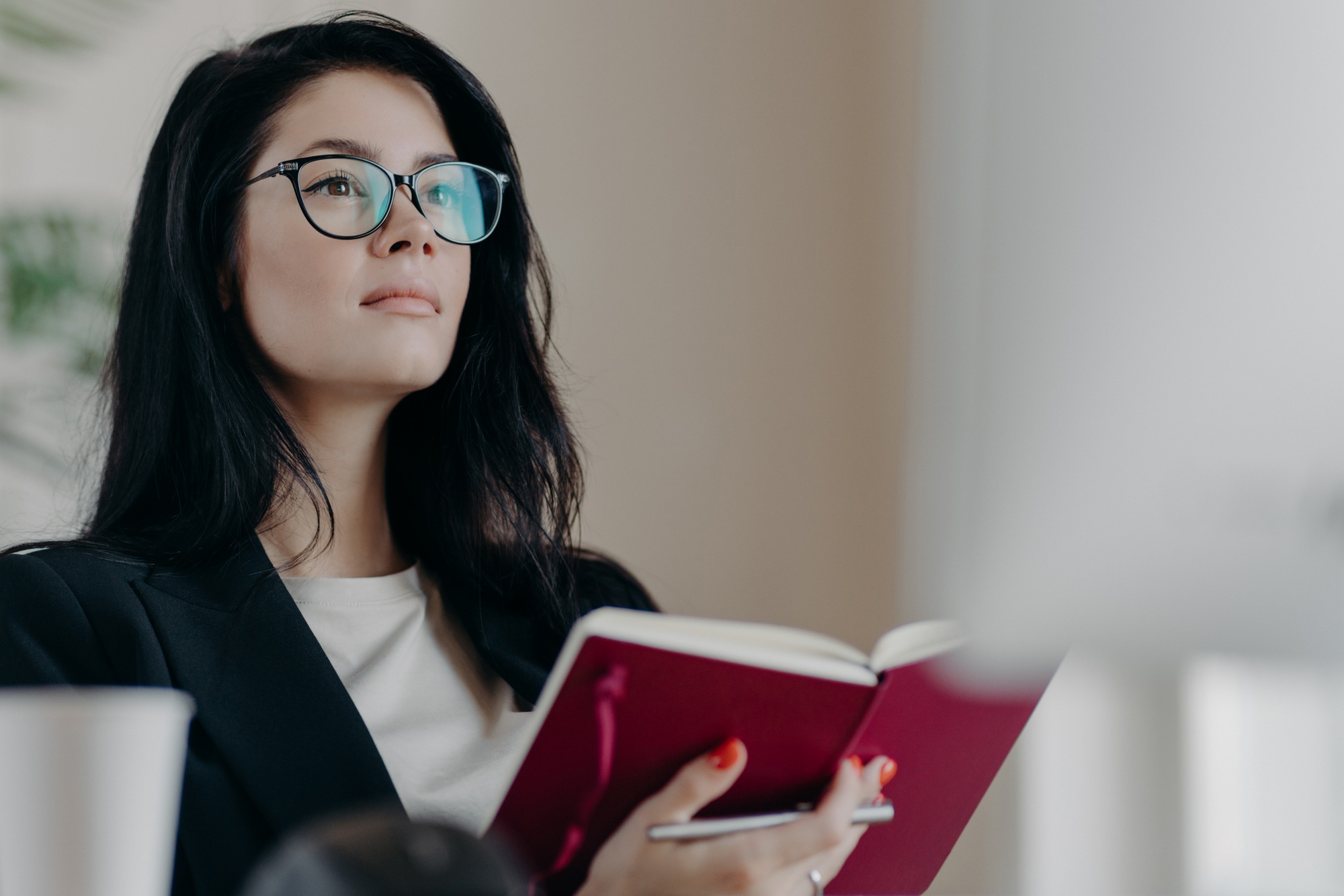 Beautiful woman with thoughtful expression, holds opened notepad, writes time management