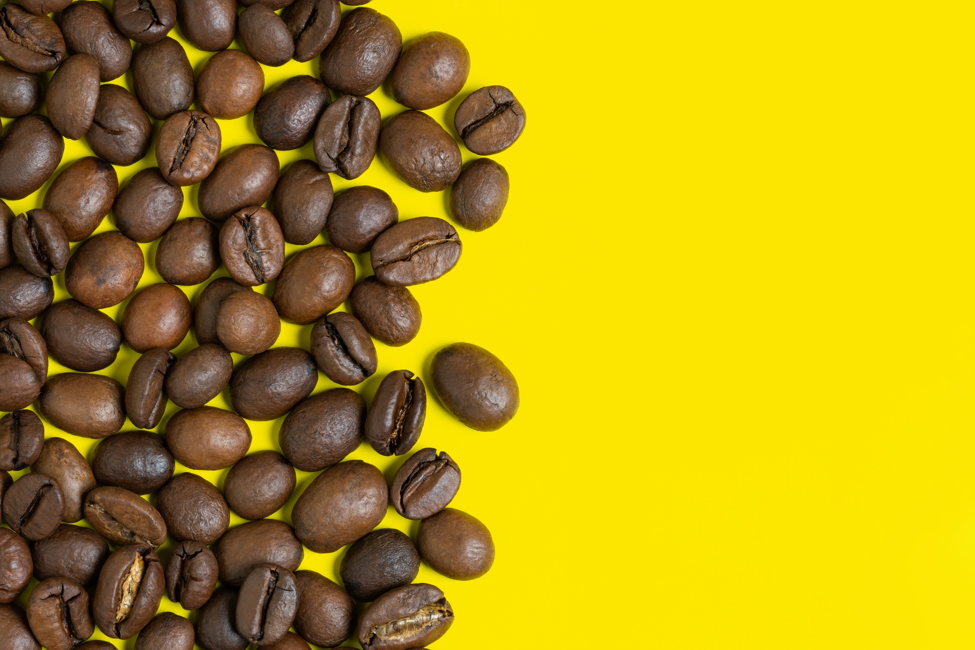 Black coffee beans on yellow background. Left vertical location objects, copy space for text on