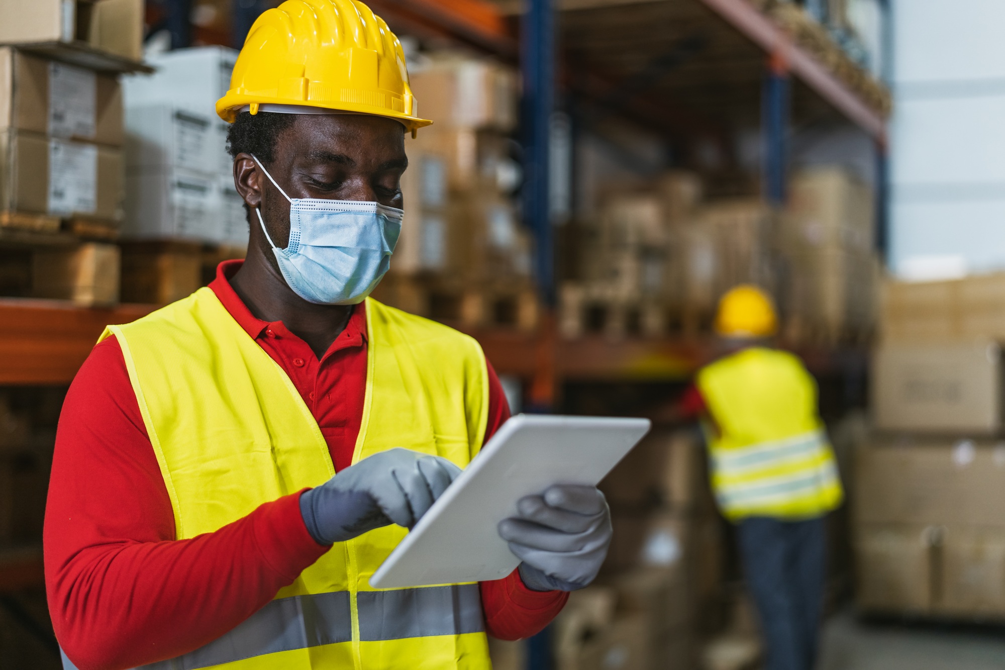 Black man working in warehouse doing inventory using digital tablet and loading delivery boxes plan