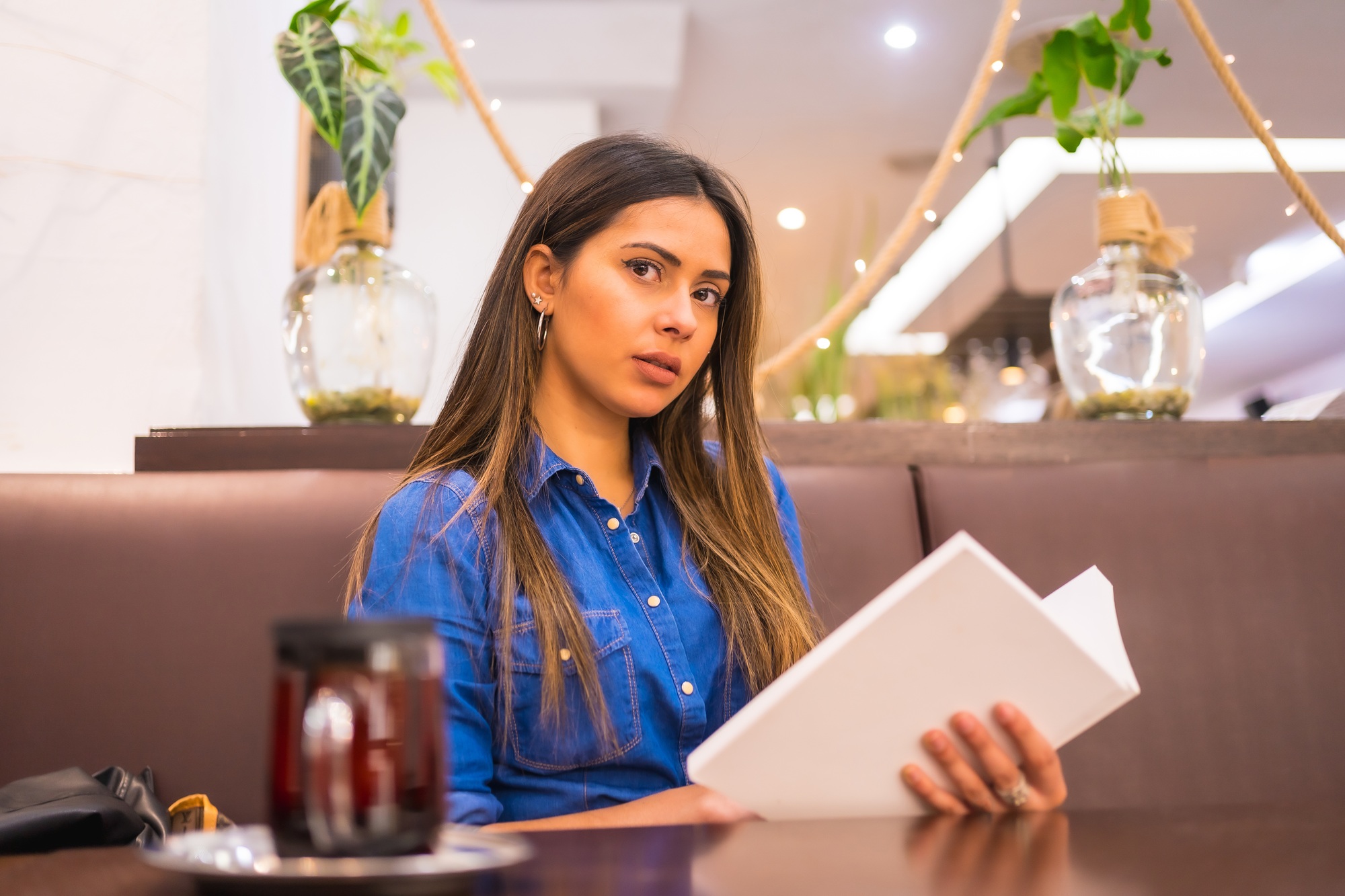 Brunette Caucasian girl in a denim shirt having tea in a coffee shop.