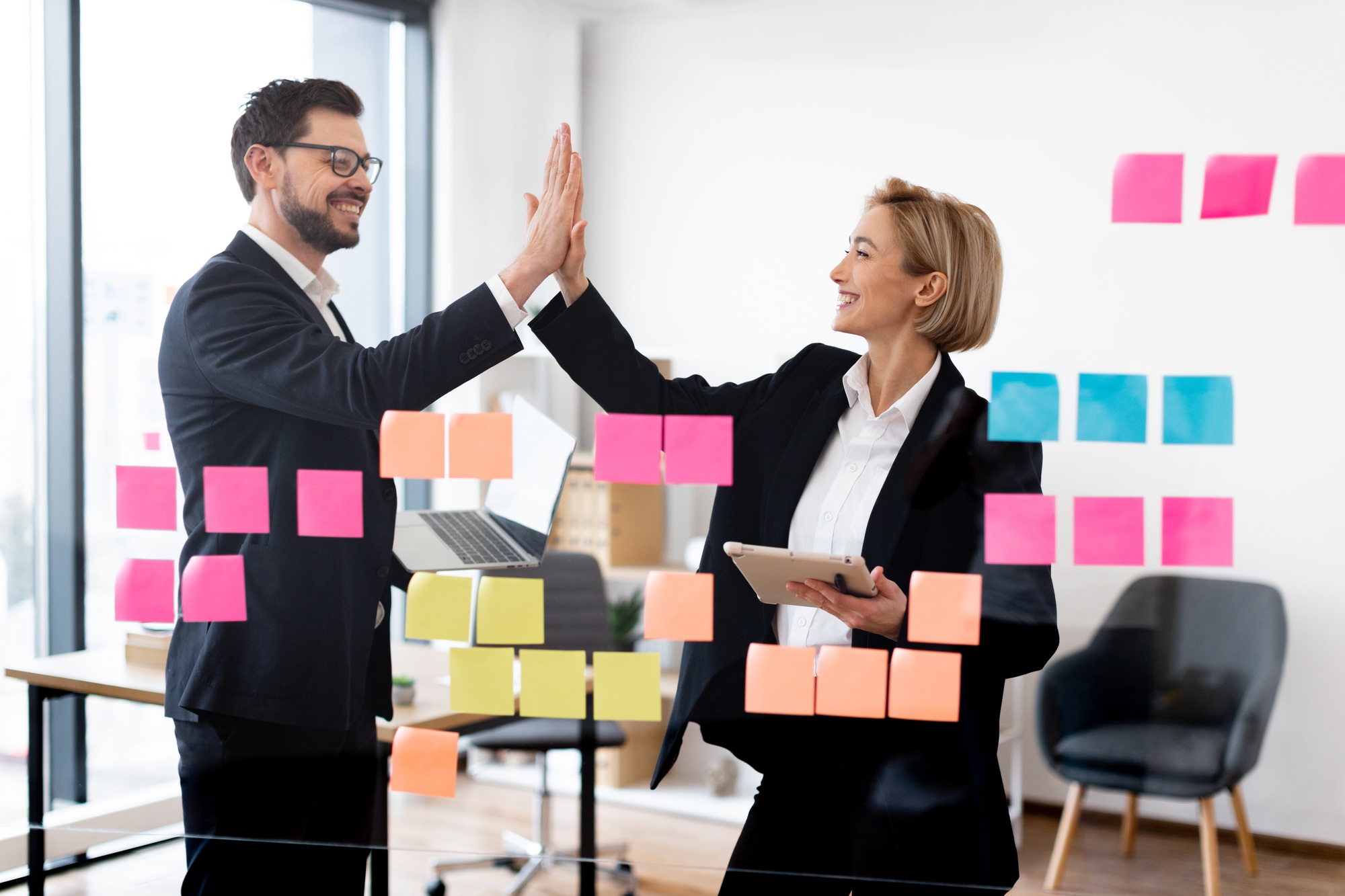 Business colleagues high-five during strategic planning with notes on board