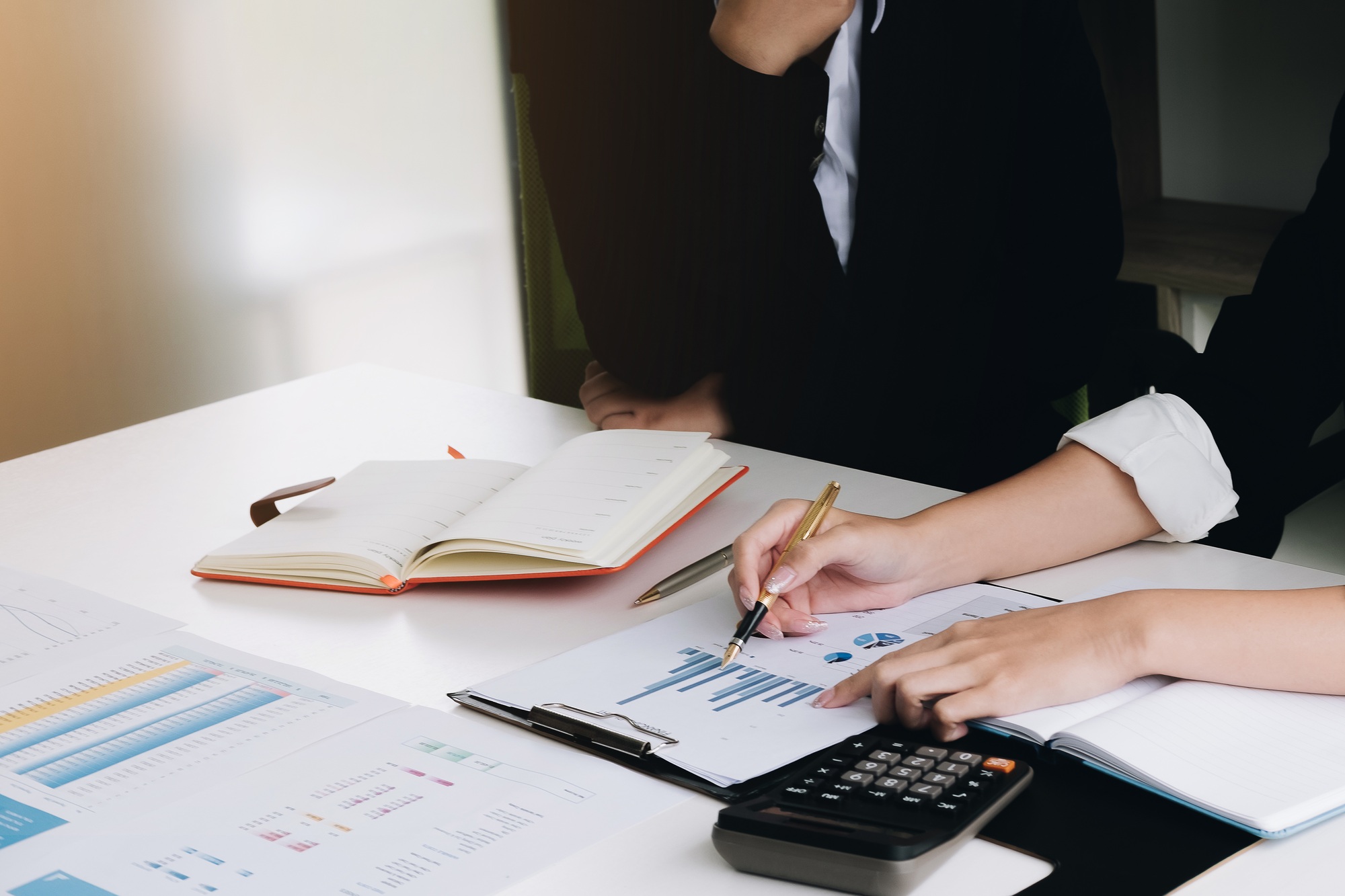 business hand holding pen and partner pointing graph chart for analyze the company's sales plan in