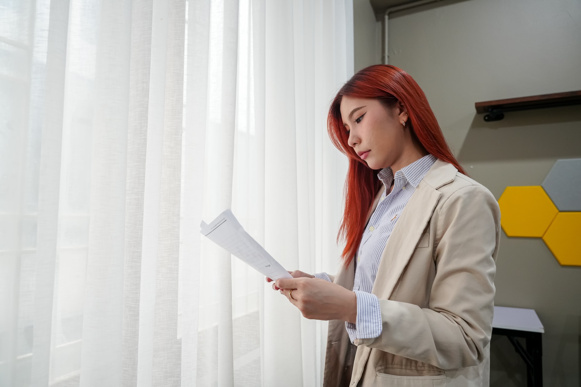 Business professional reviewing documents by the window in a modern office setting