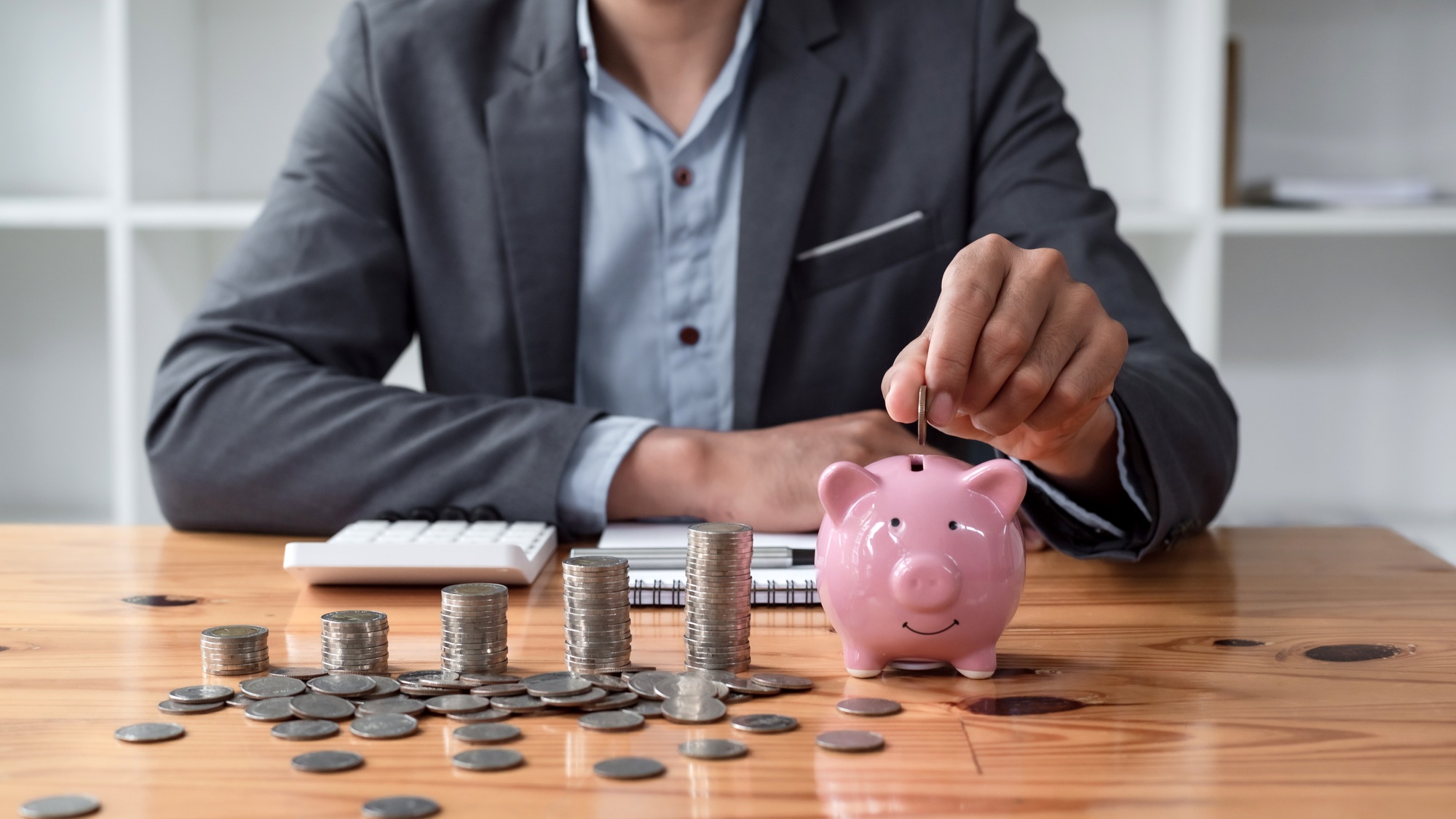 Businessman saving money with piggy bank and coins on desk