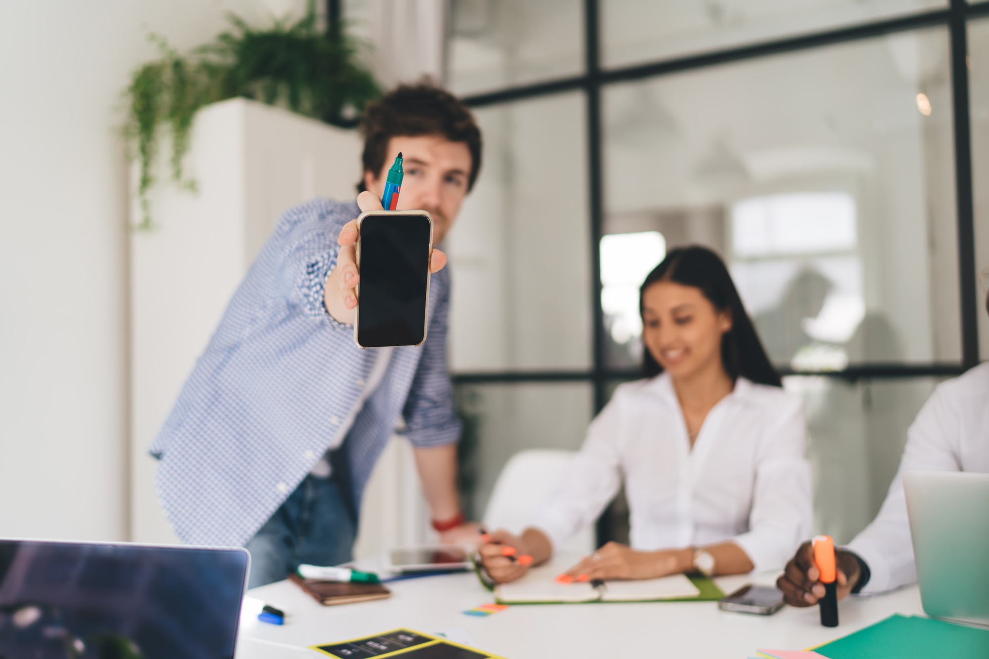 Businessman showing smartphone screen while standing near colleagues in office