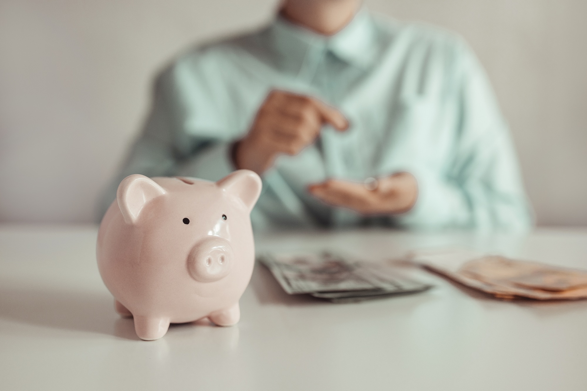 Businesswoman considers a bundle of dollar money. Piggy bank on a white table.