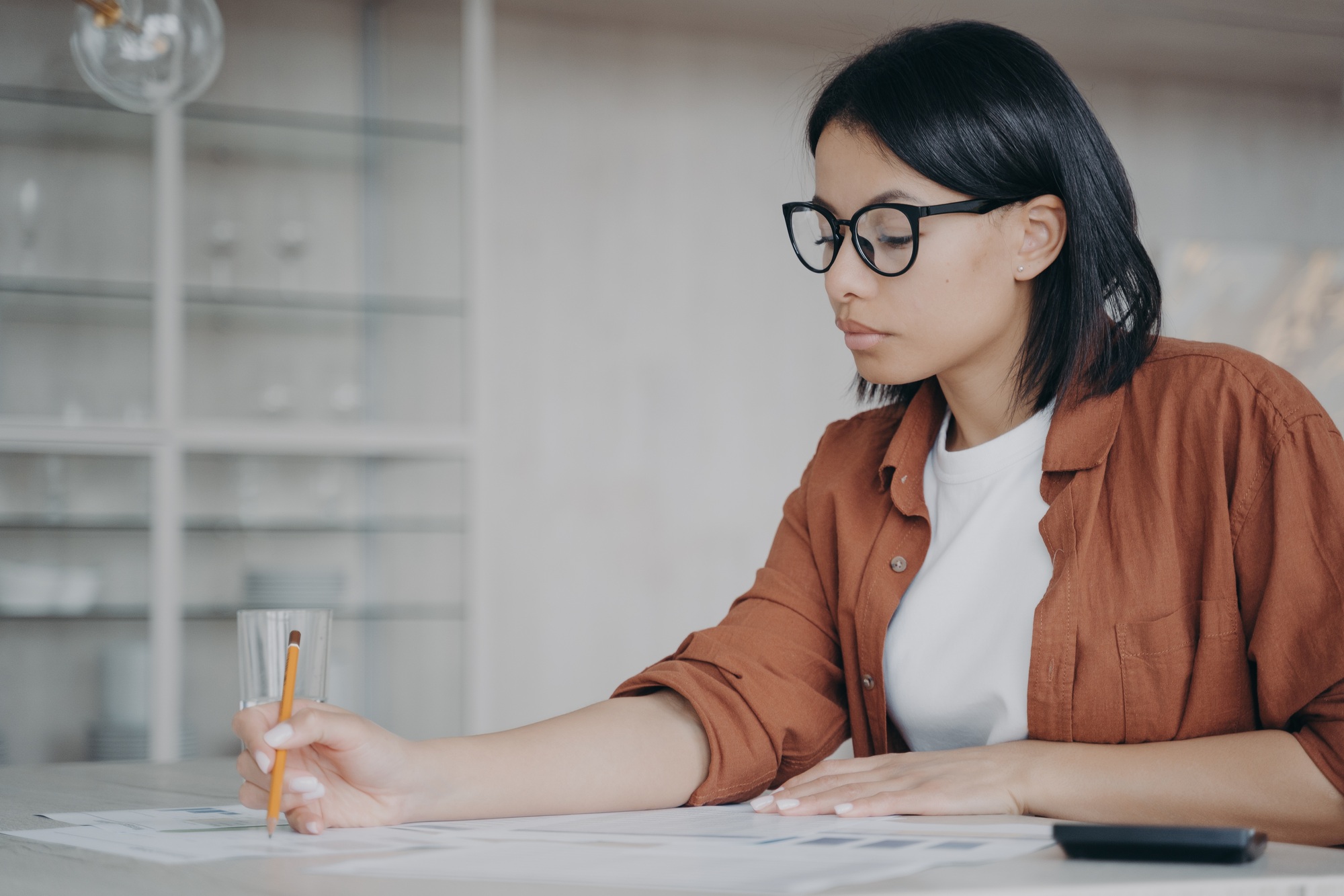 Businesswoman in glasses calculates monthly expenses, taxes sitting at workplace desk in office