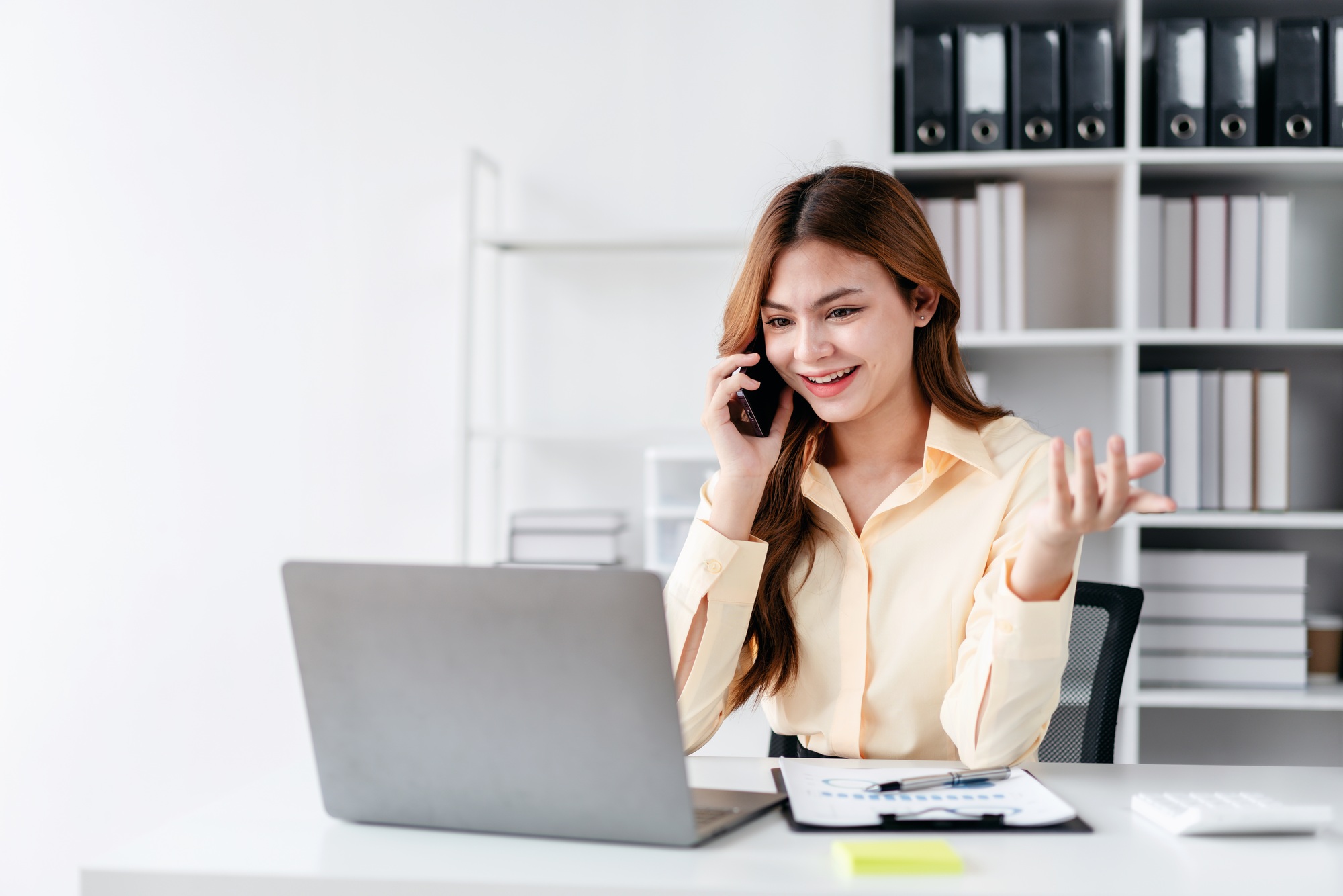 Businesswoman talking on smartphone while working and reading business marketing plan report