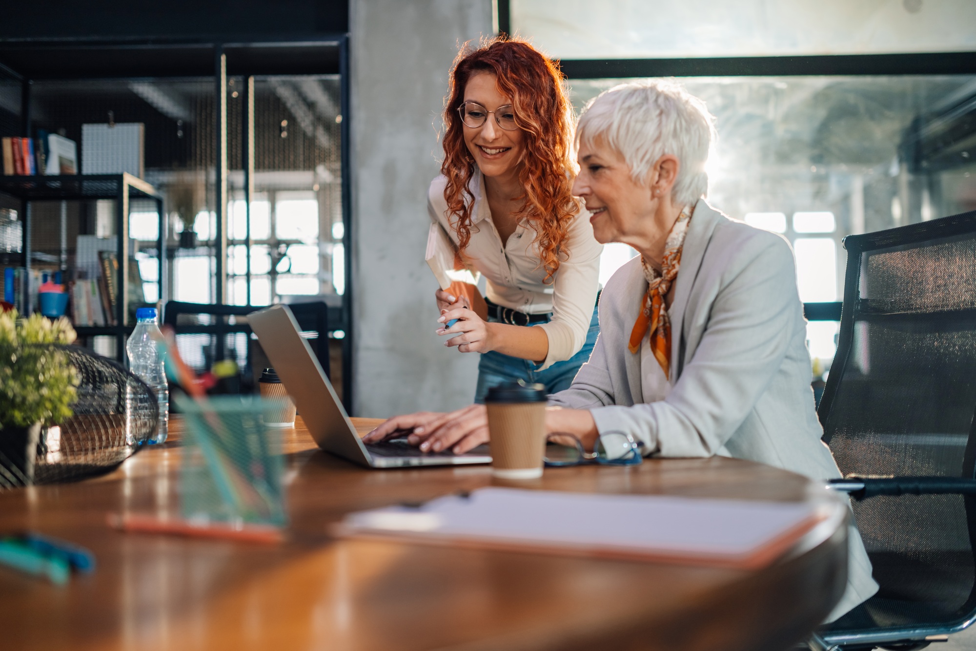 Businesswoman typing report on laptop and collaborating with colleague