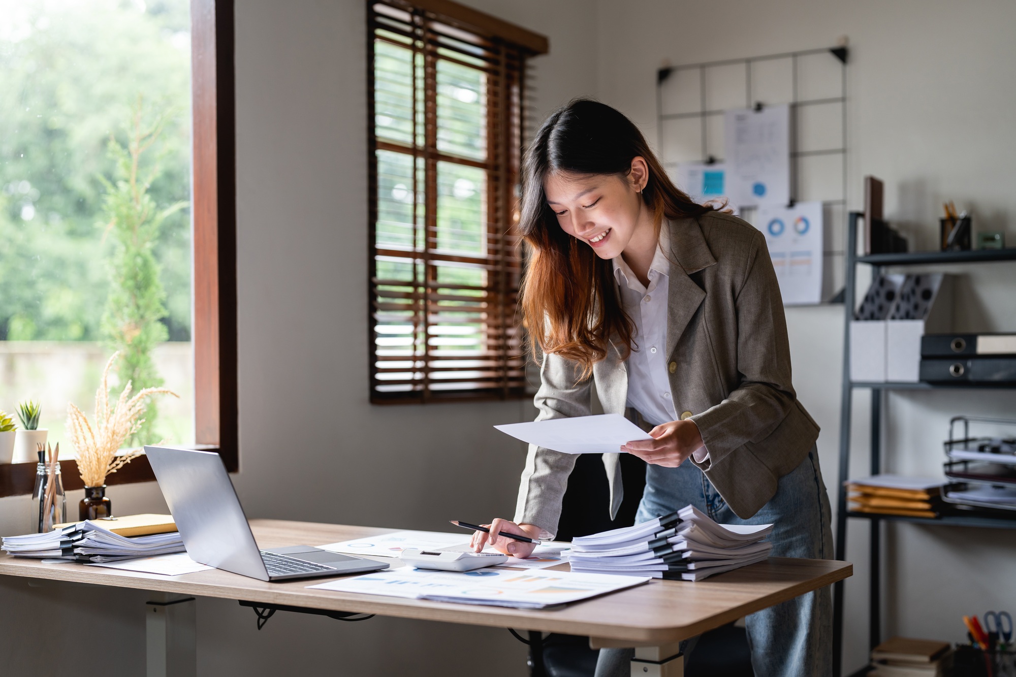 businesswoman using calculator holding papers preparing report analyzing work results, female