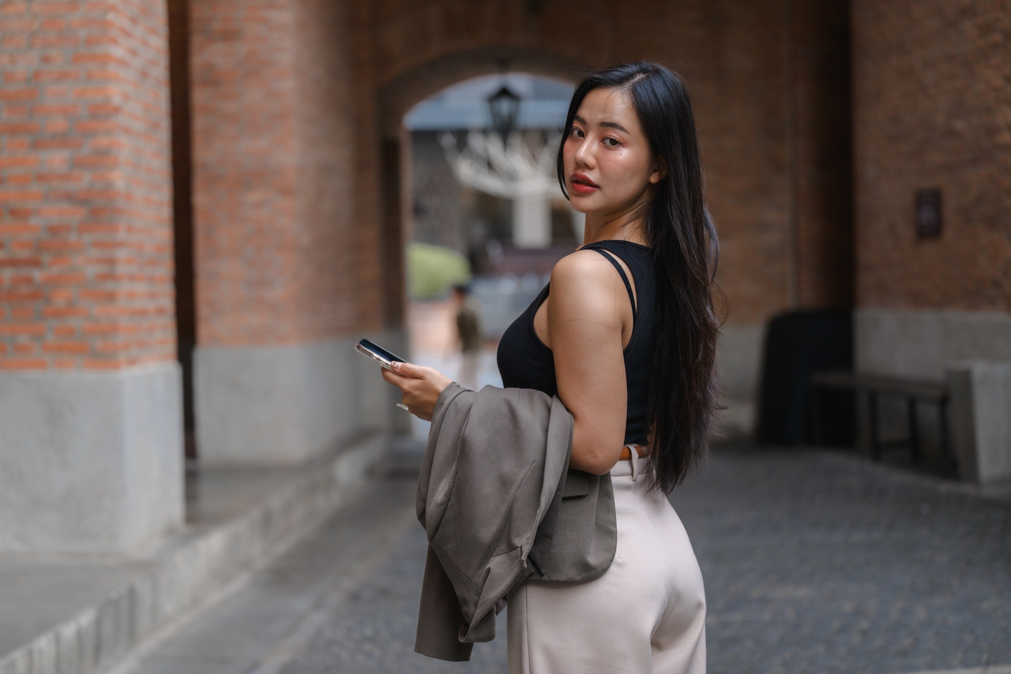 Businesswoman walking in urban setting holding smartphone and jacket