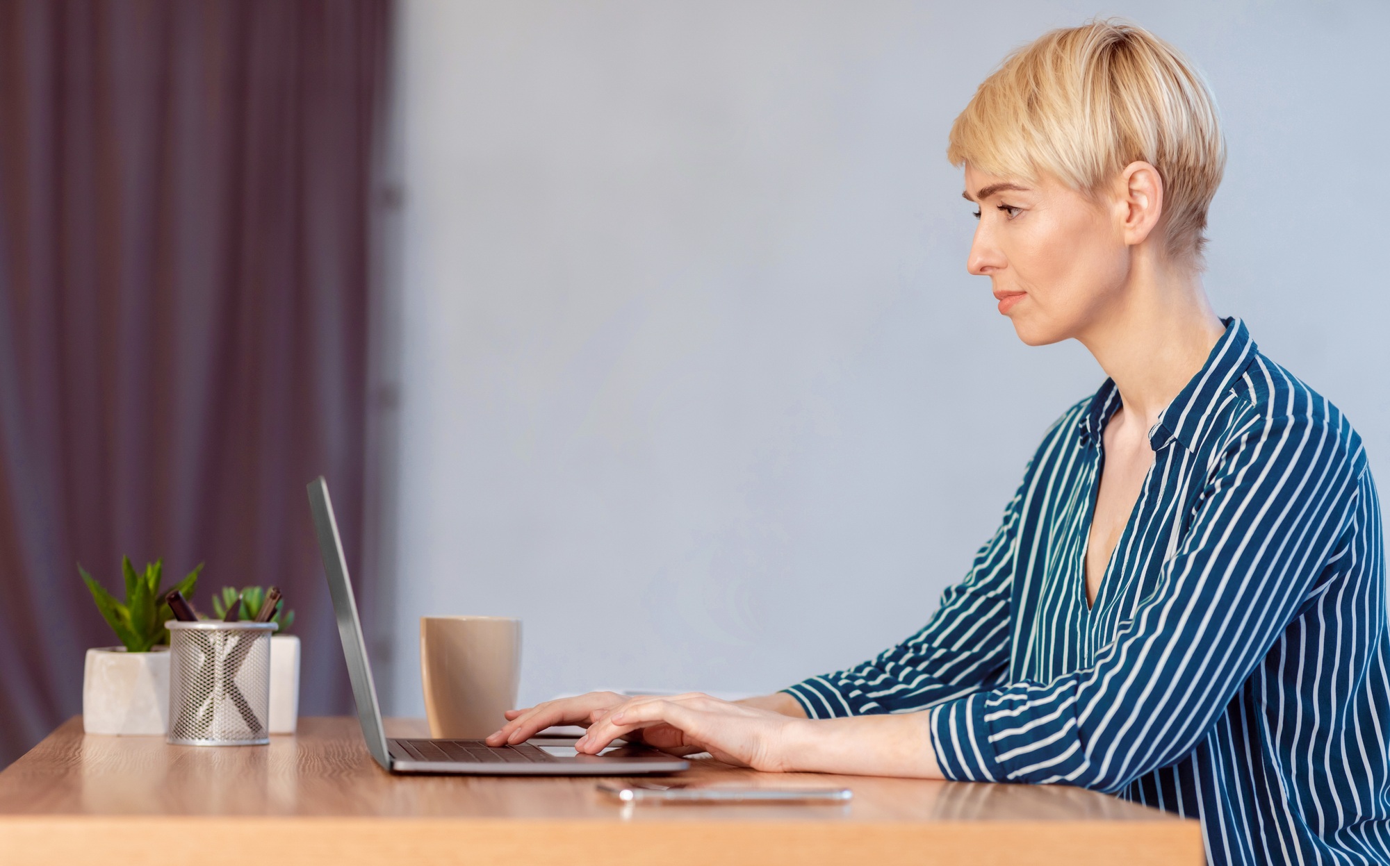 Businesswoman Working On Laptop Typing Financial Report In Office, Side-View