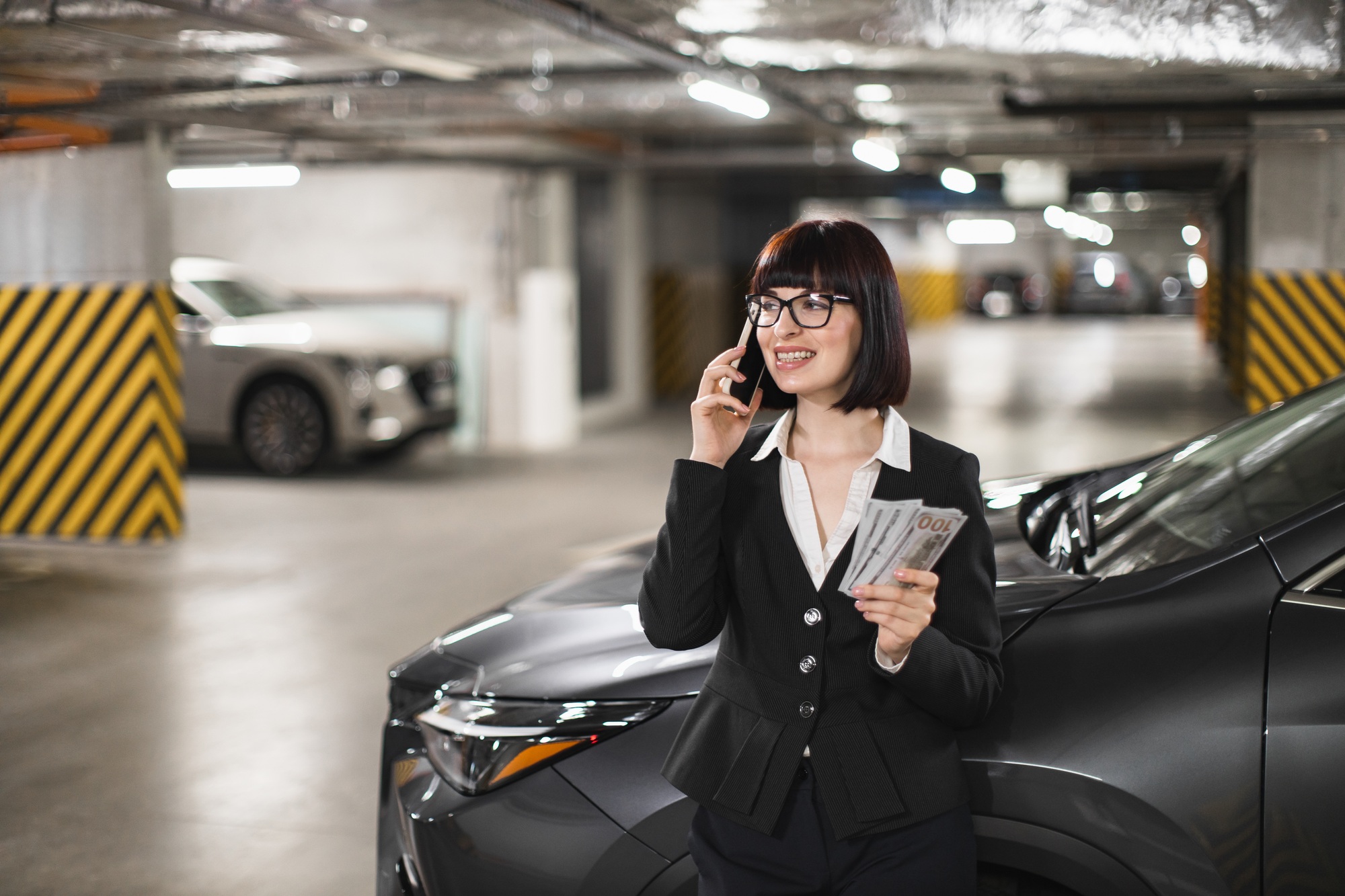 Caucasian businesswoman talking on phone in parking lot holding cash